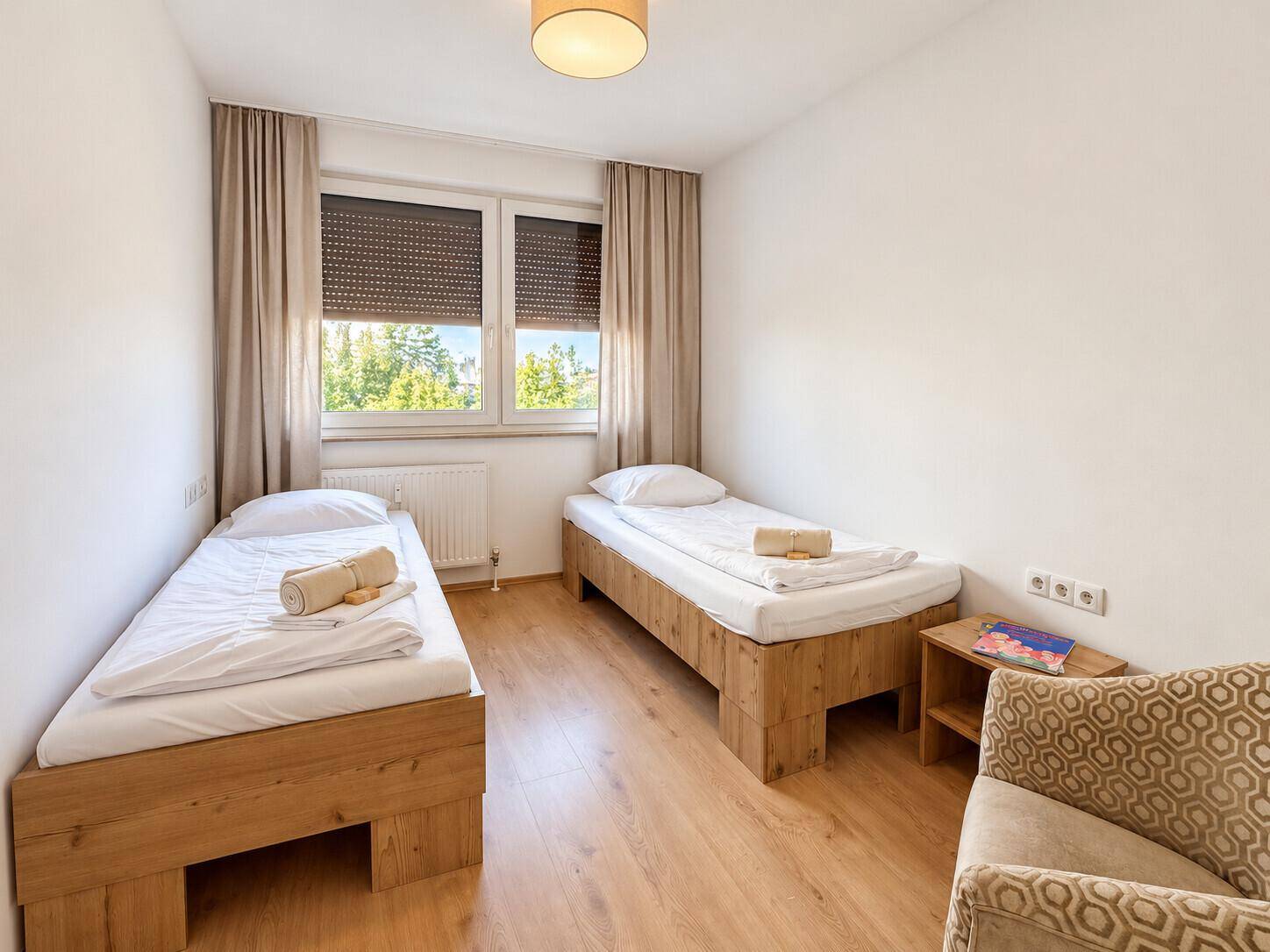 Helles Schlafzimmer mit zwei Einzelbetten, Fenster und Nachttisch.