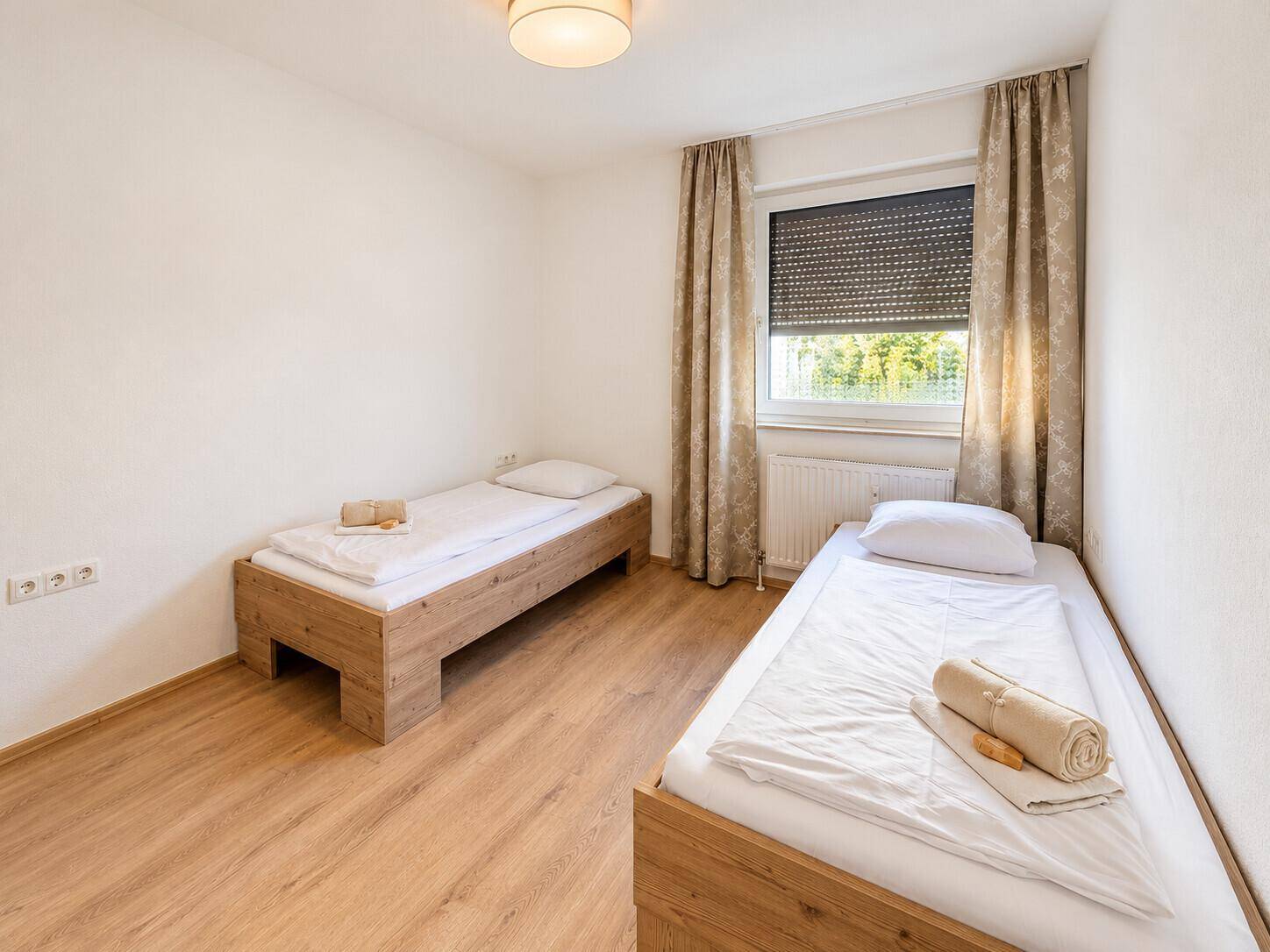 Schlafzimmer mit zwei Einzelbetten, Fenster und hellem Laminatboden.