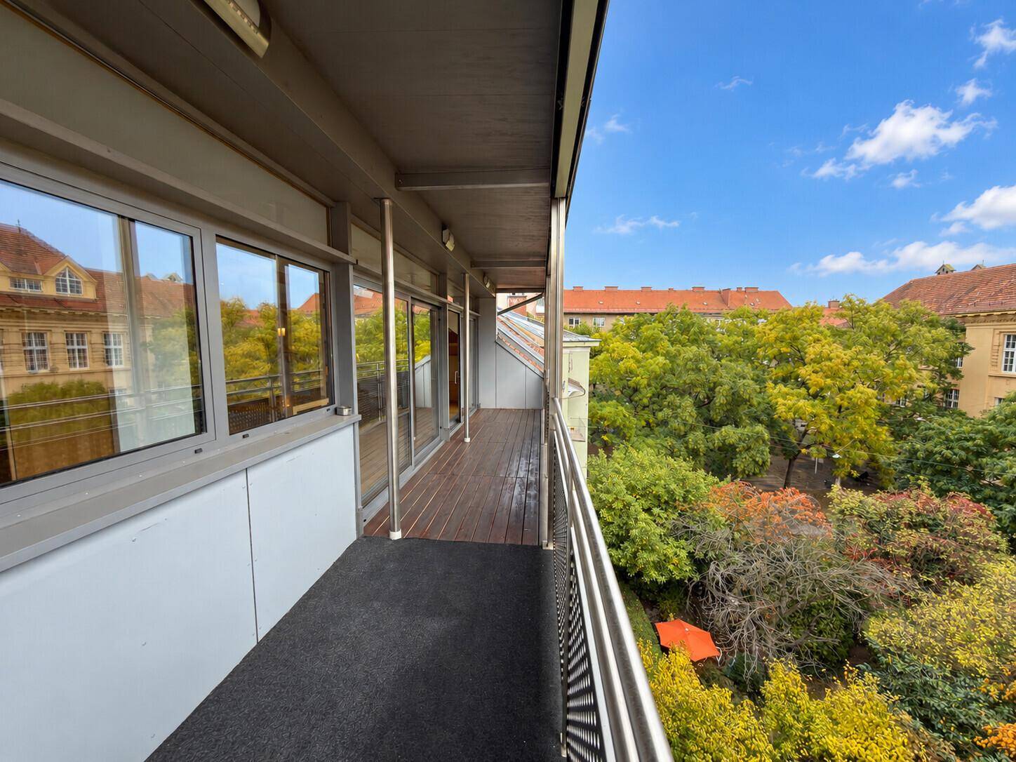 Langer Balkon mit Holzboden und Metallgeländer, bietet einen grünen Blick auf die Umgebung.