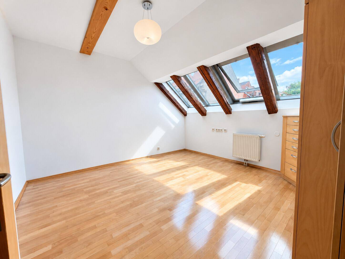 Lichtdurchflutetes Schlafzimmer mit Dachschrägen, Holzbalken und großzügigen Dachfenstern.
