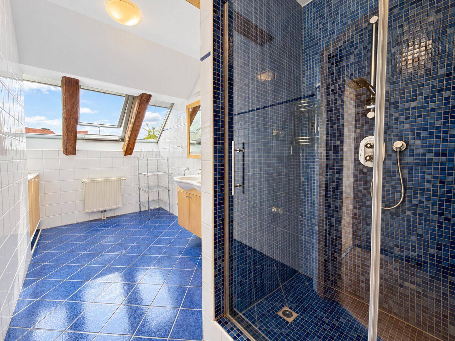 Modernes Badezimmer mit blauen Mosaikfliesen, Duschkabine und Dachfenster.