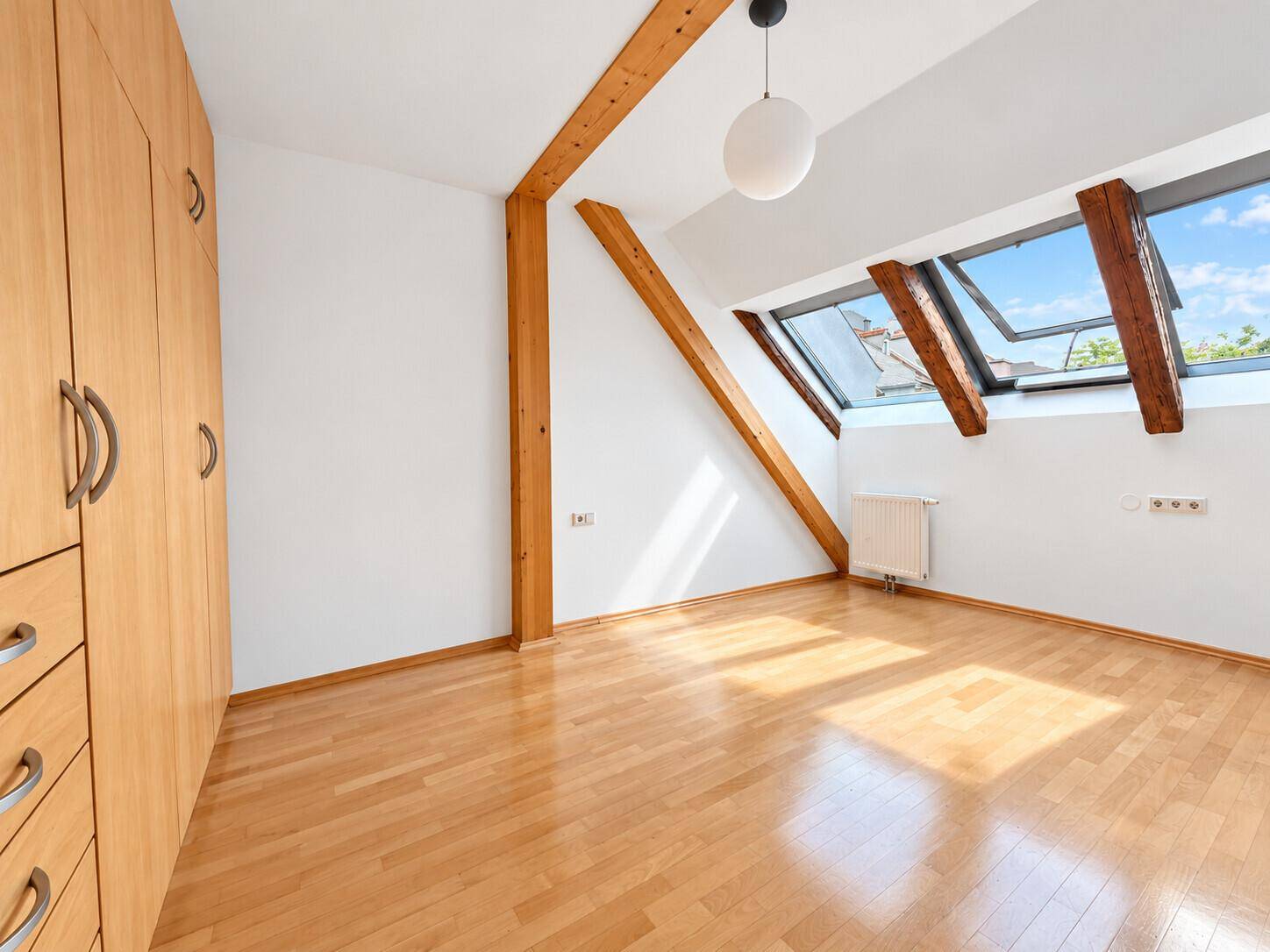 Helles Schlafzimmer im Dachgeschoss mit Holzbalken, Parkettboden und Dachfenstern.