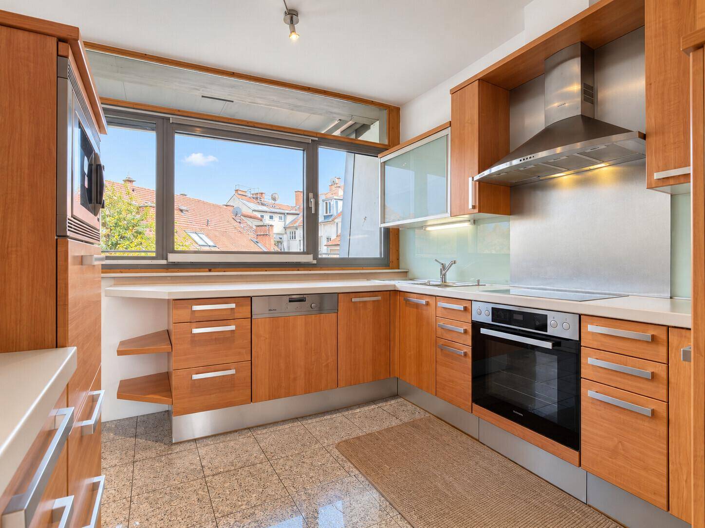 Funktionale Küche mit Holzschränken, modernen Geräten und einem großen Fenster.