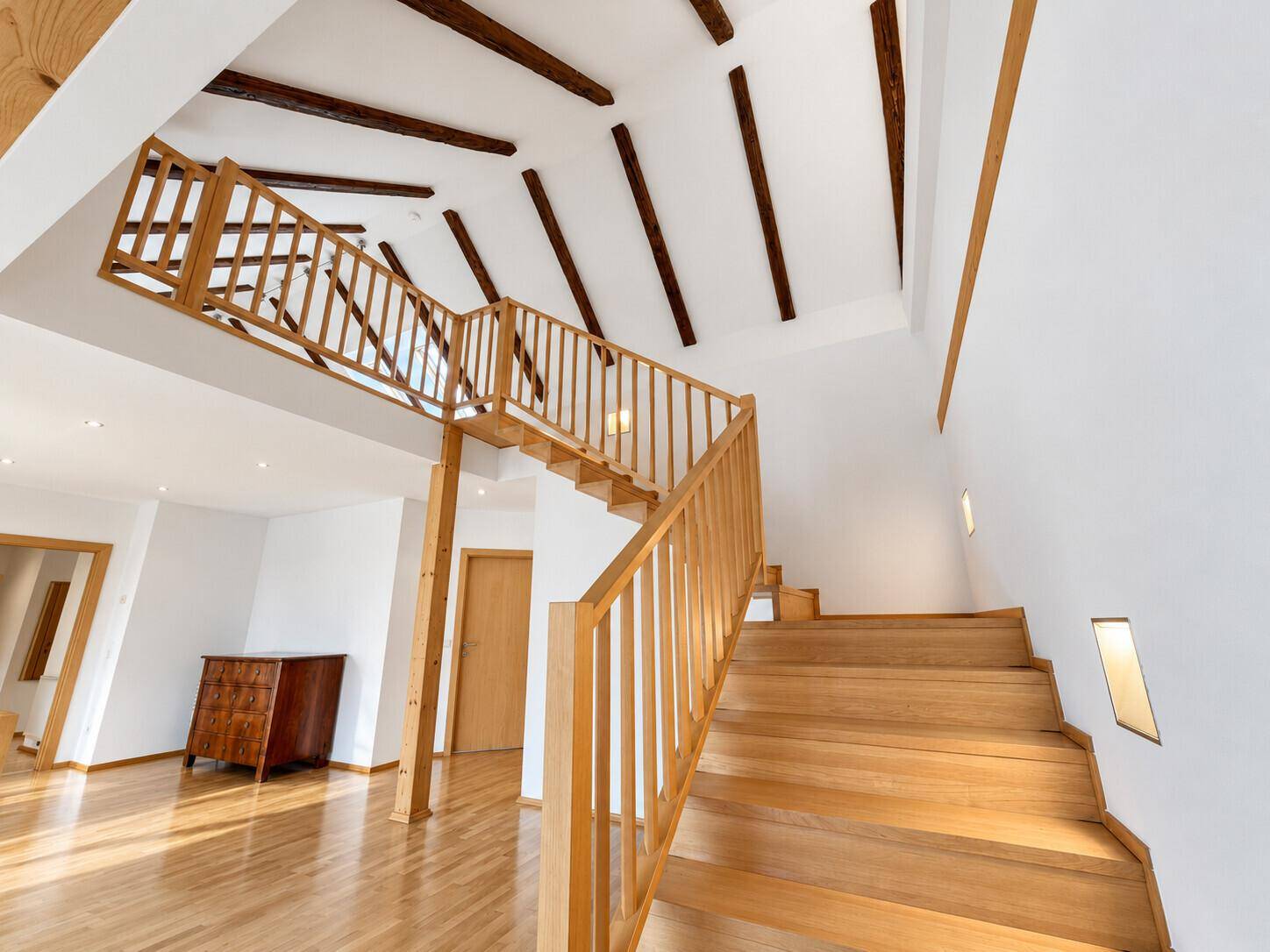 Offener Wohnbereich mit beeindruckender Holztreppe, hohen Decken und sichtbaren Holzbalken.