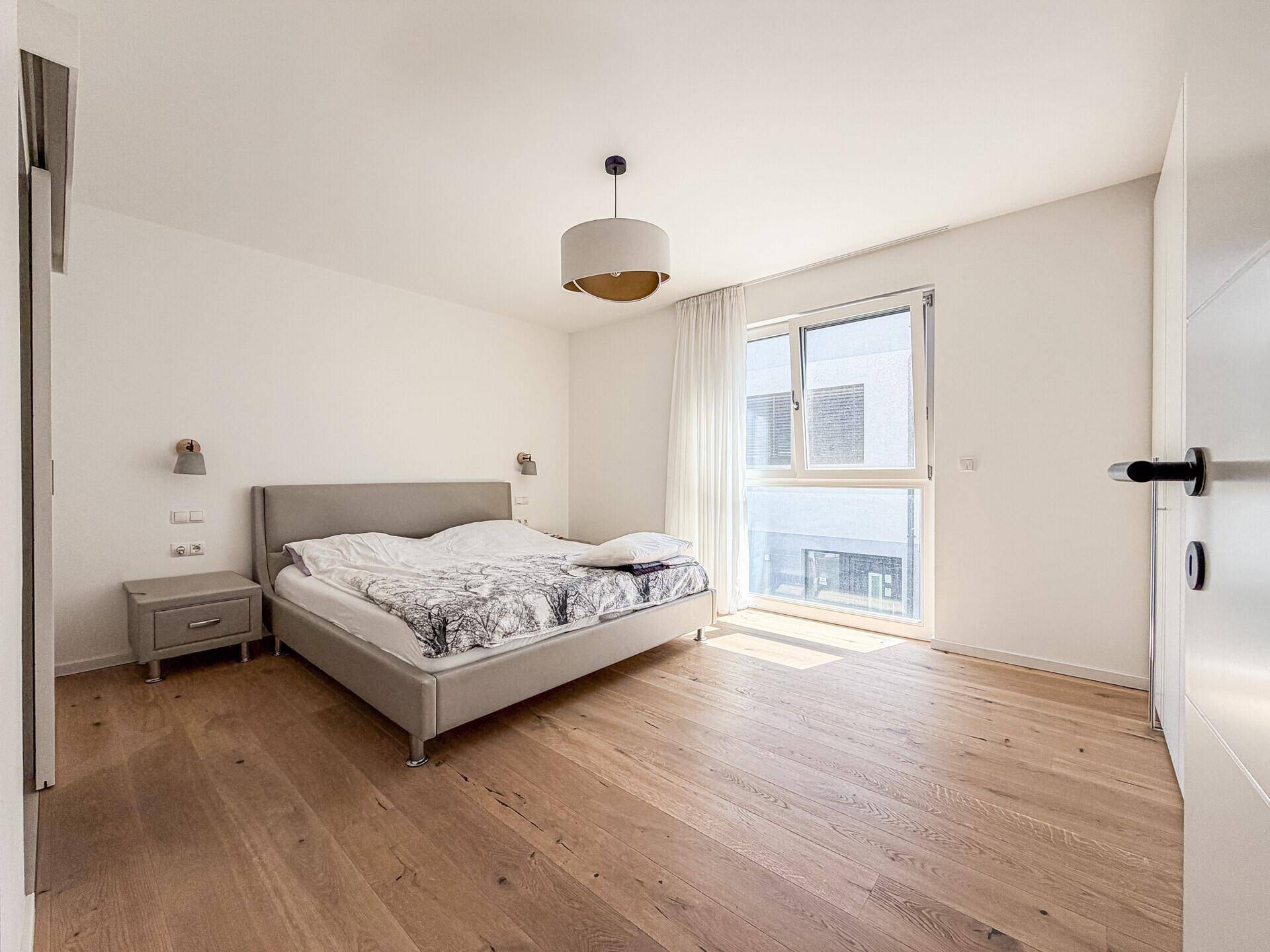 Helles Schlafzimmer mit Holzboden, großem Fenster und modernem Bett.