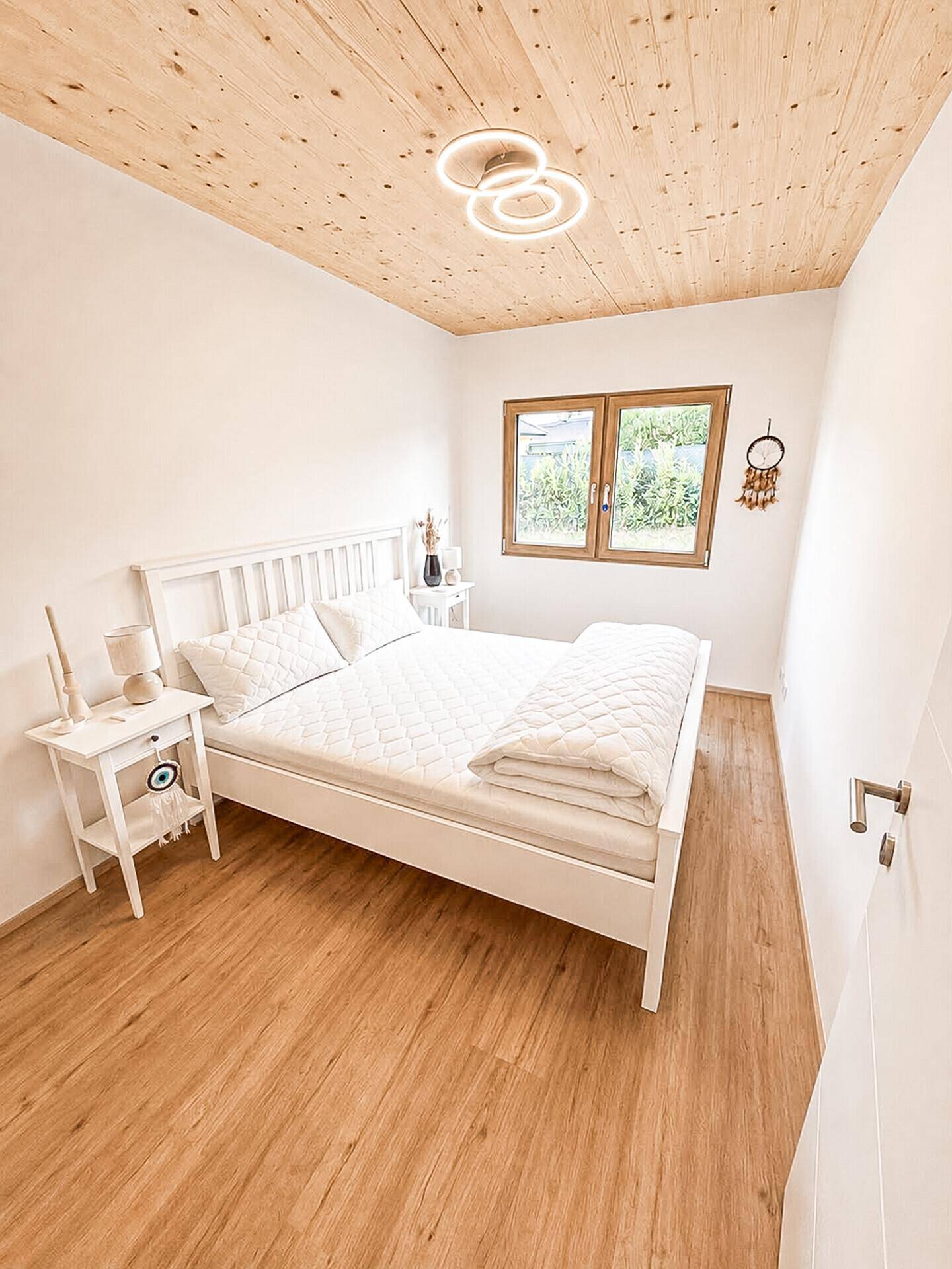 Helles Schlafzimmer mit Holzboden, Holzdecke und weißem Bett, modern und freundlich eingerichtet.