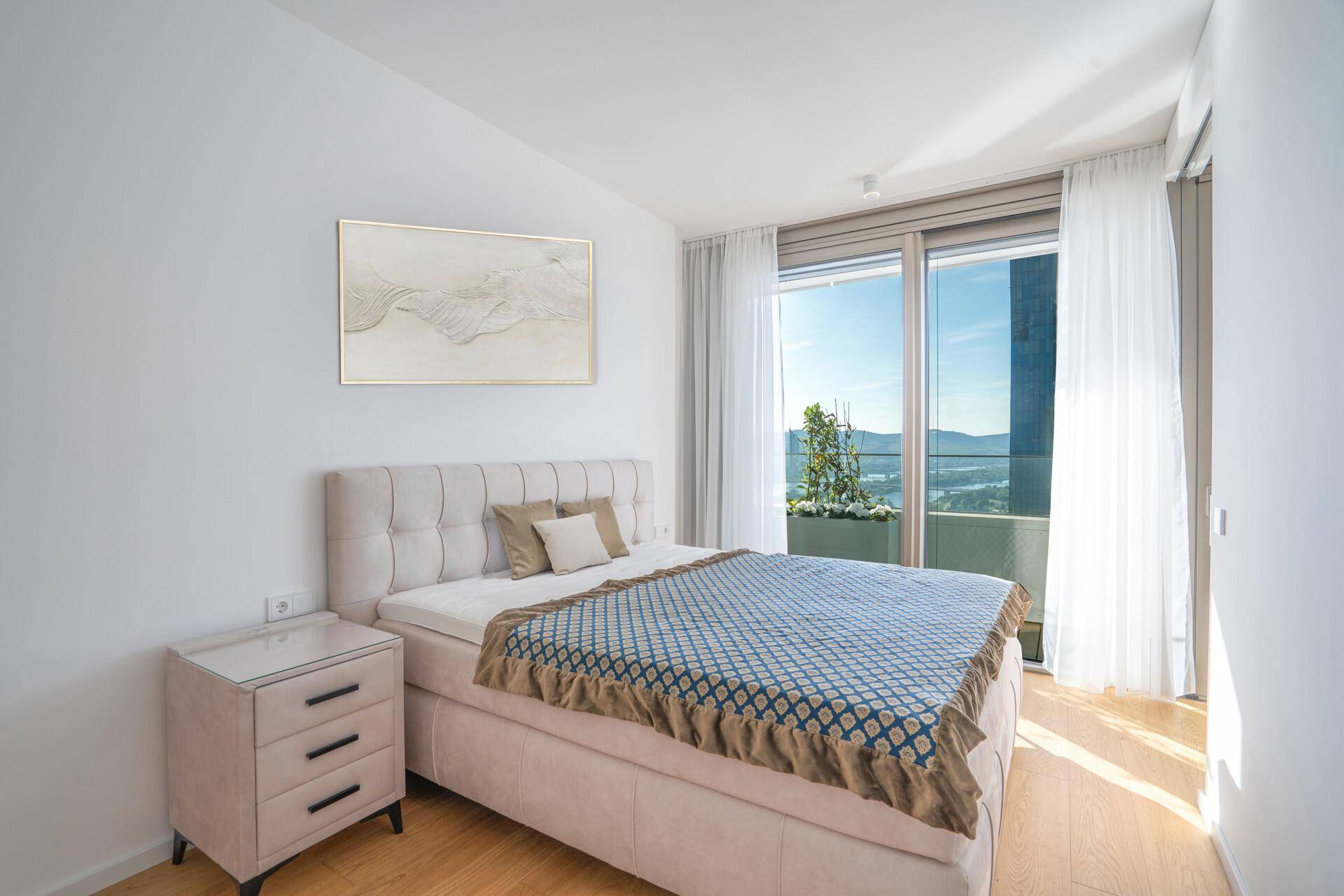 Gemütliches Schlafzimmer mit großem Bett, Nachttisch und bodentiefen Fenstern mit Zugang zum Balkon.