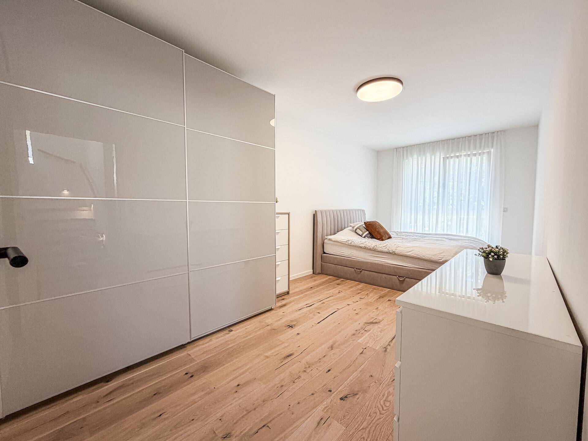 Geräumiges Schlafzimmer mit Holzboden, großem Kleiderschrank und viel Tageslicht.