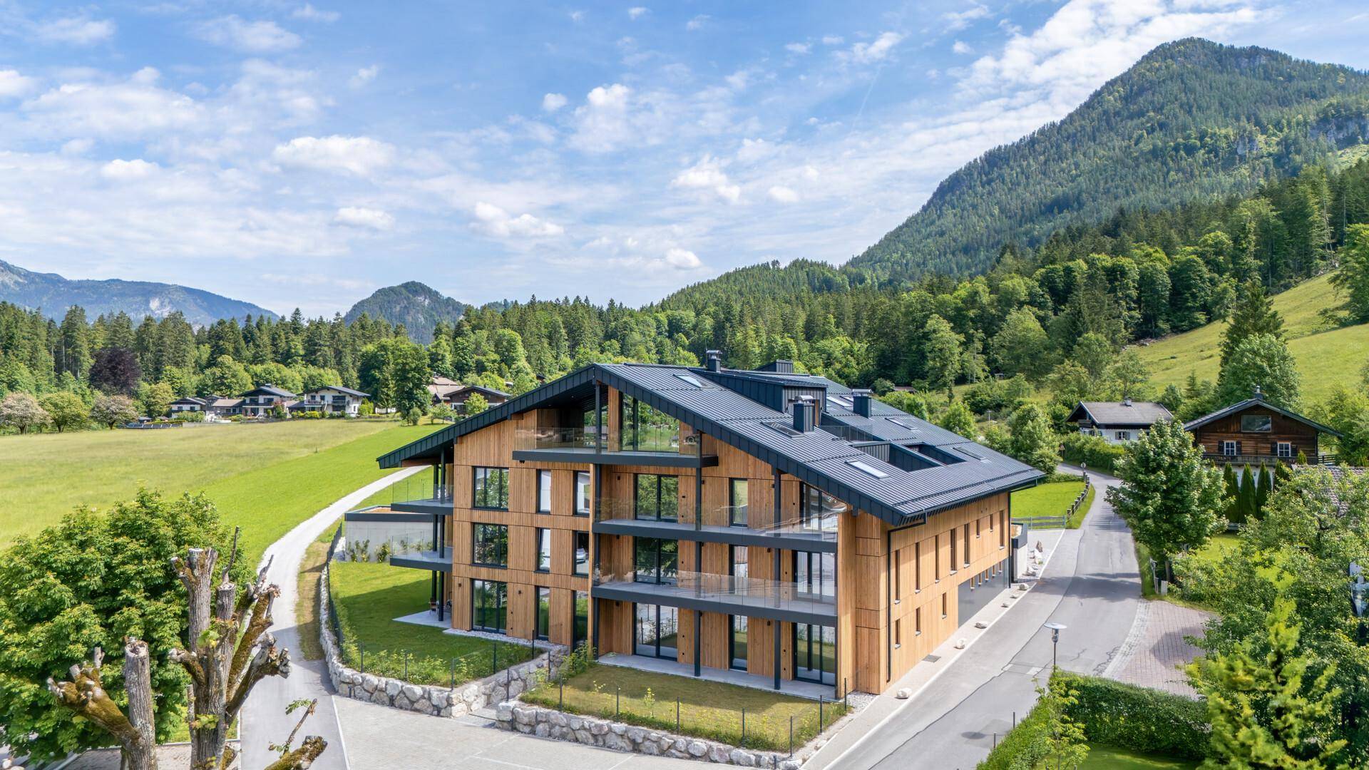 Modernes Apartmentgebäude mit Holzfassade und großen Fenstern in alpiner Landschaft.