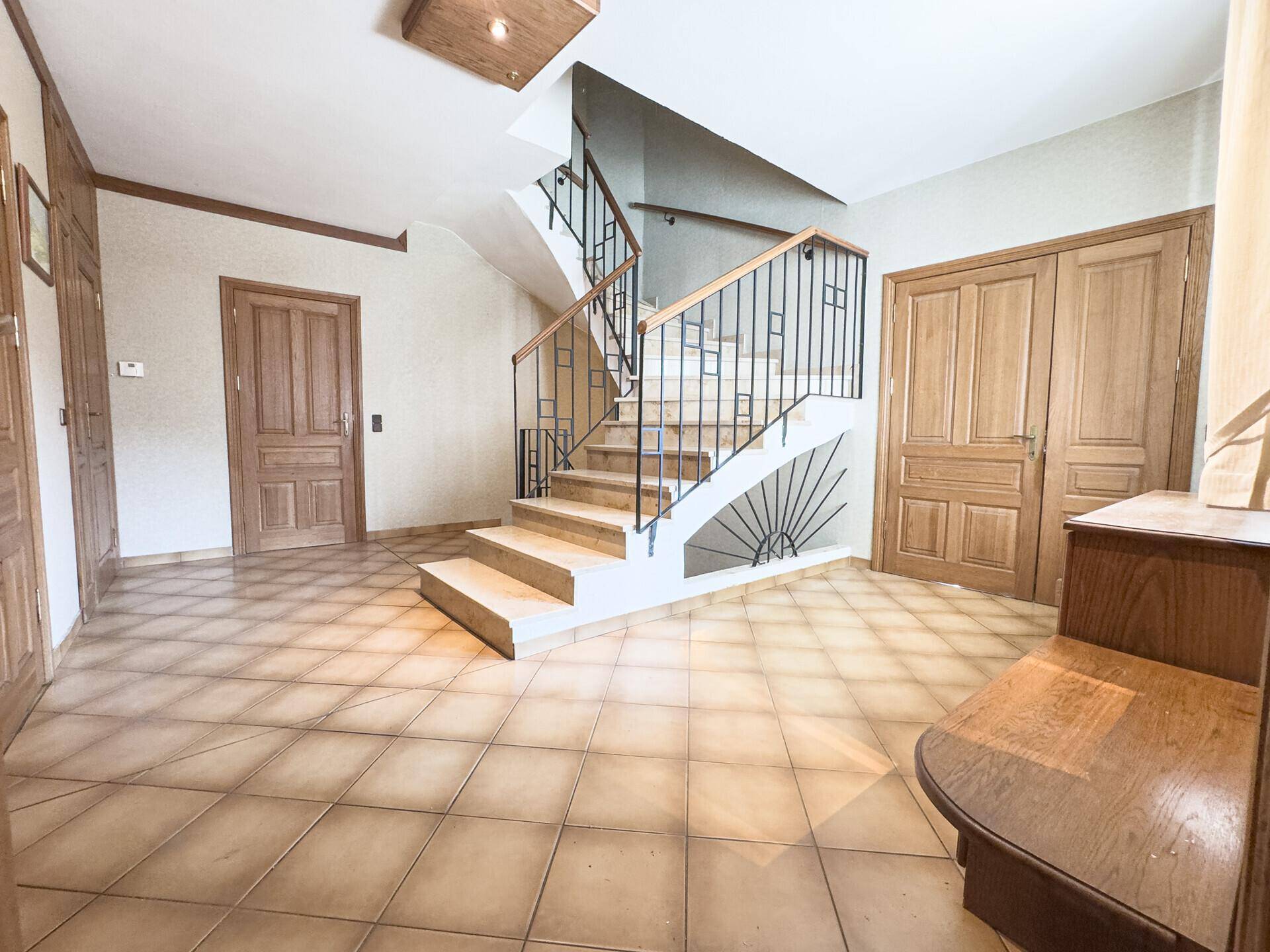 Geräumiger Eingangsbereich mit einer geschwungenen Treppe, Fliesenboden und Holztüren.
