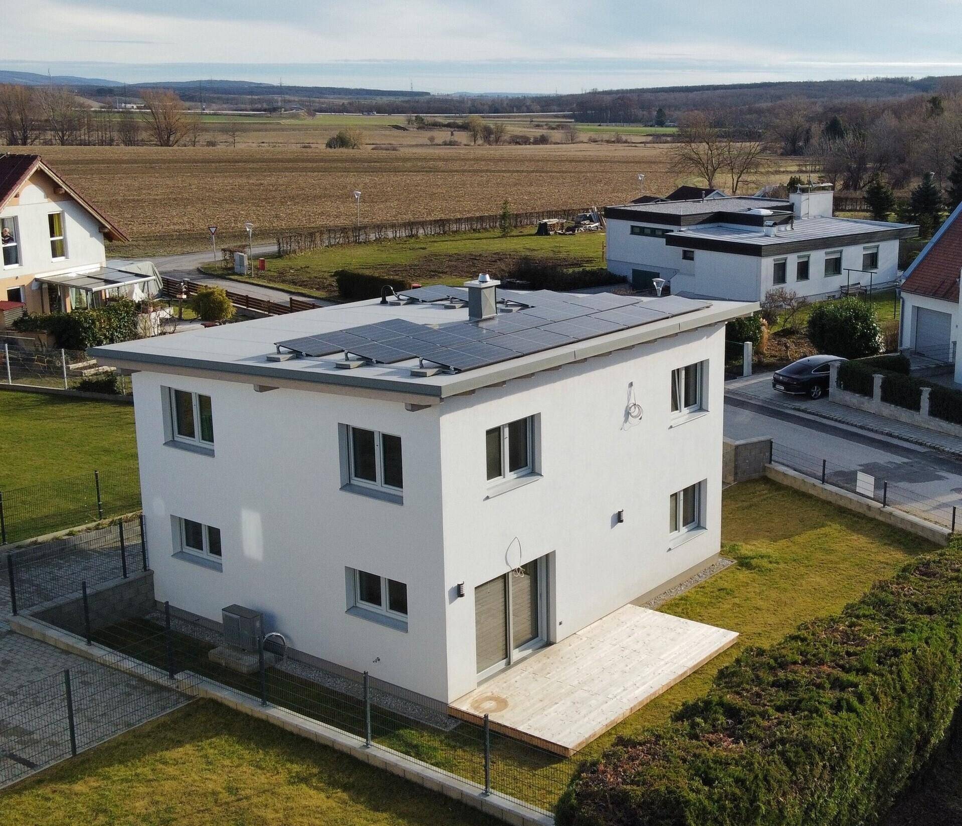 Luftaufnahme eines modernen Einfamilienhauses mit Flachdach, Photovoltaikanlage und Garten in ländlicher Umgebung.