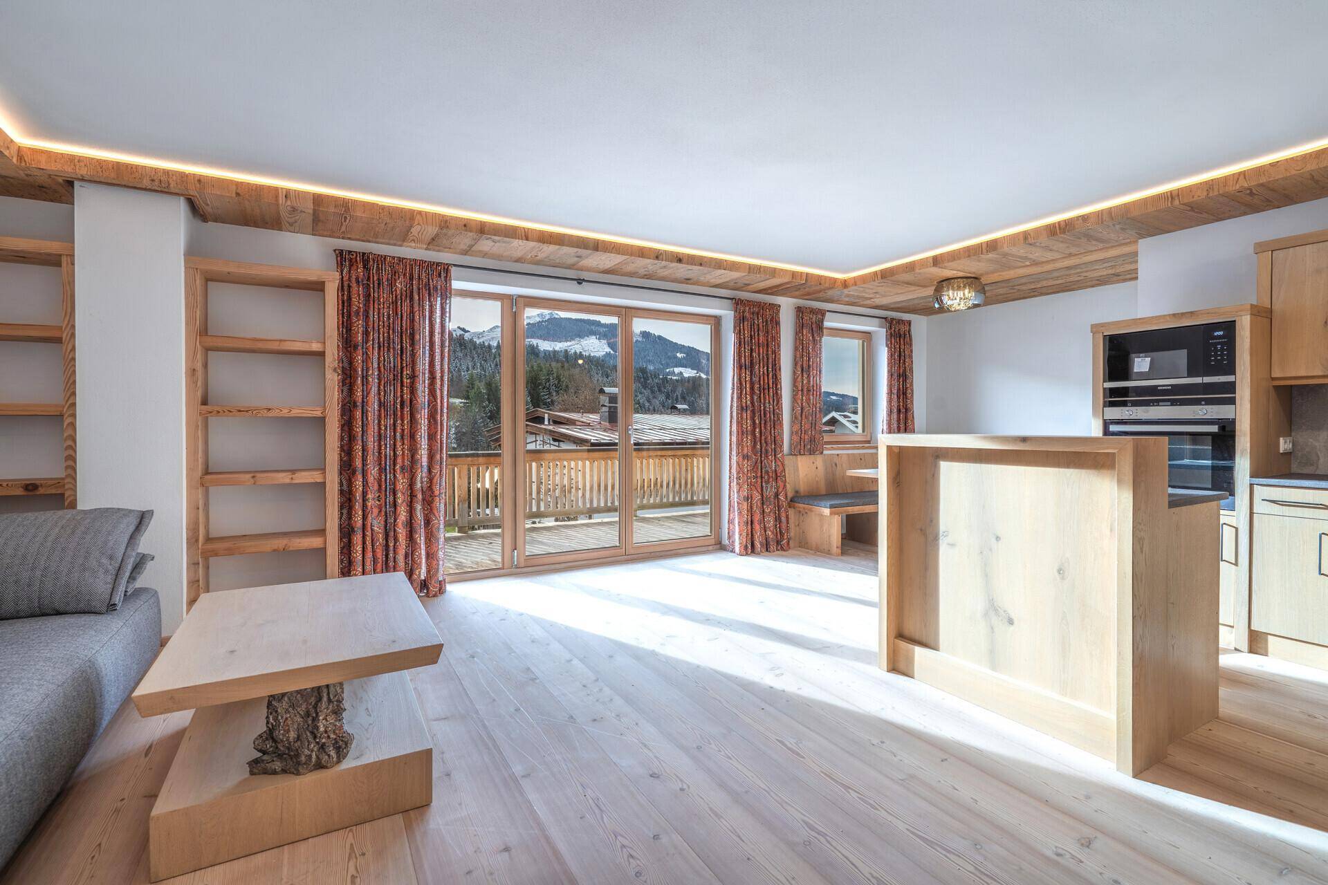 Heller Wohnbereich mit Holzböden, integrierter Küche und Zugang zu einem Balkon mit Bergblick.