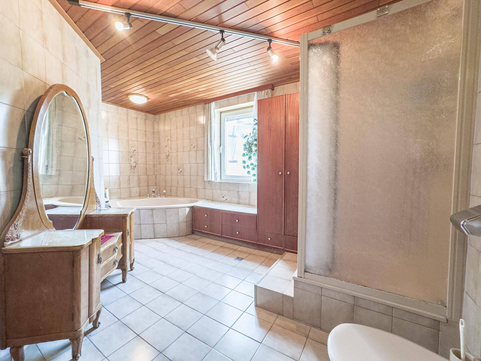 Geräumiges Badezimmer mit Fliesen, Eckbadewanne, Duschkabine und Holzdecke.