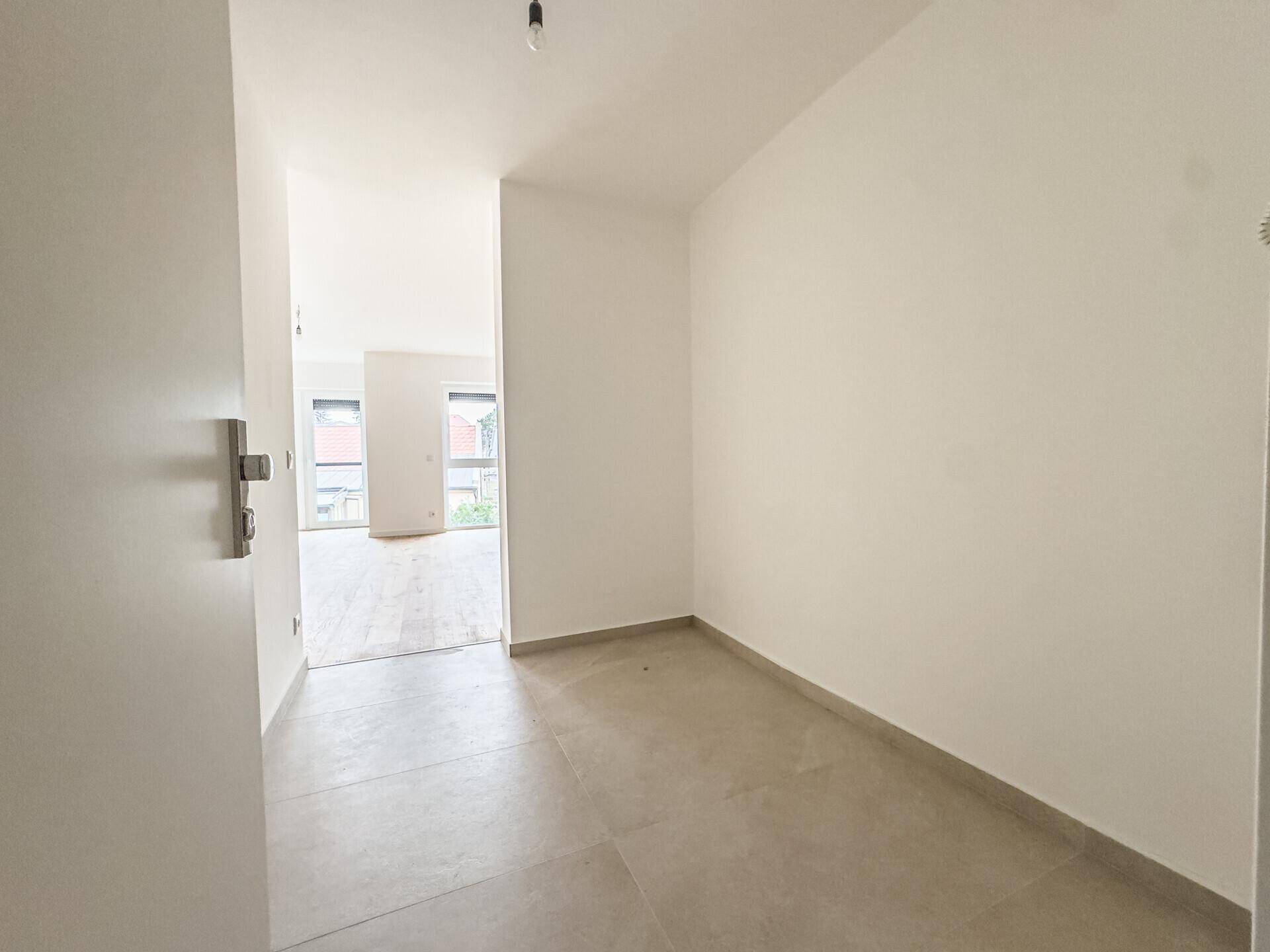 Gefliester Flur führt in einen hellen Wohnbereich mit Holzboden und großen Fenstern.
