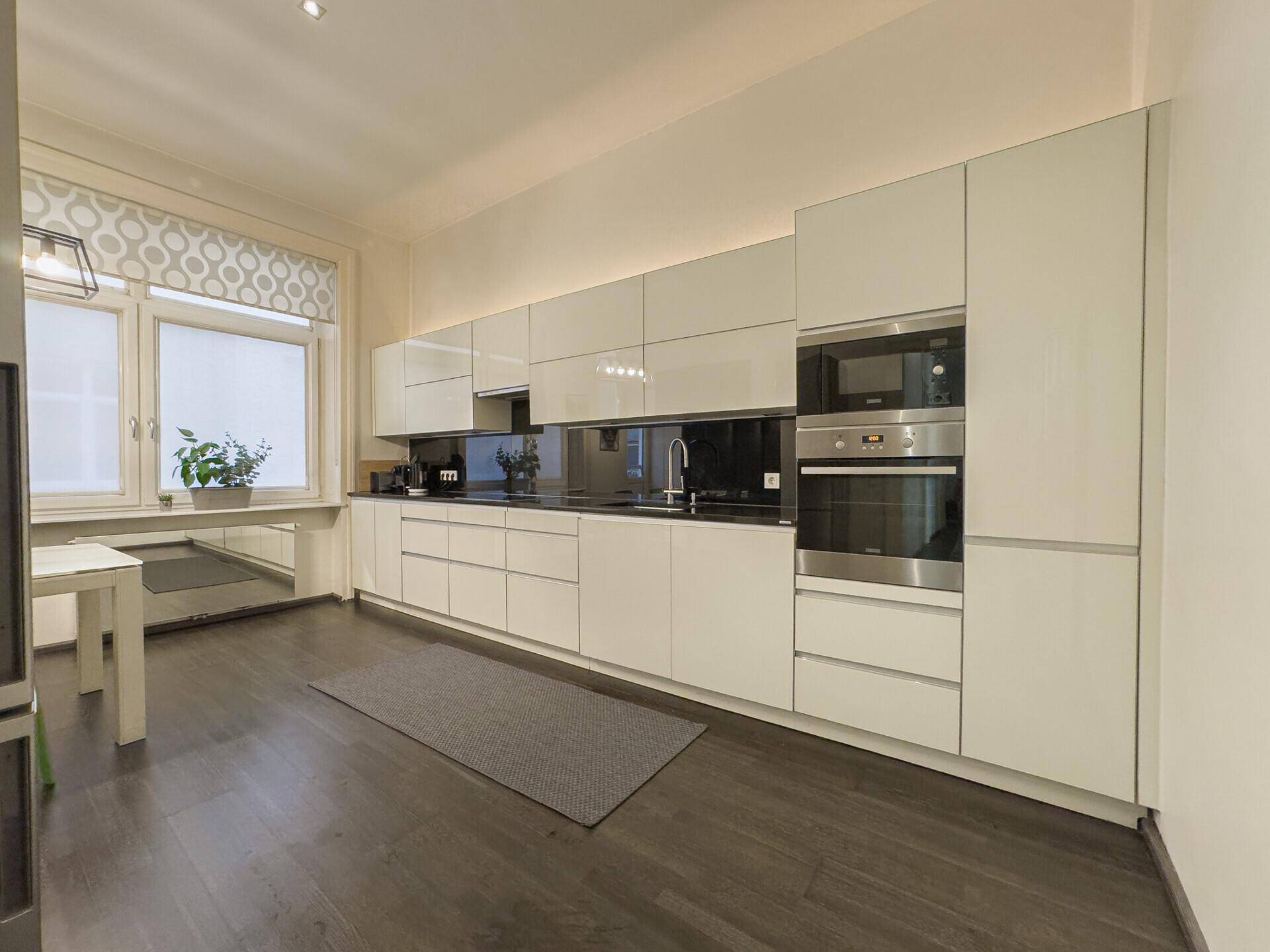 Moderne Einbauküche mit weißen Hochglanzfronten, integrierten Geräten und dunkler Arbeitsplatte.