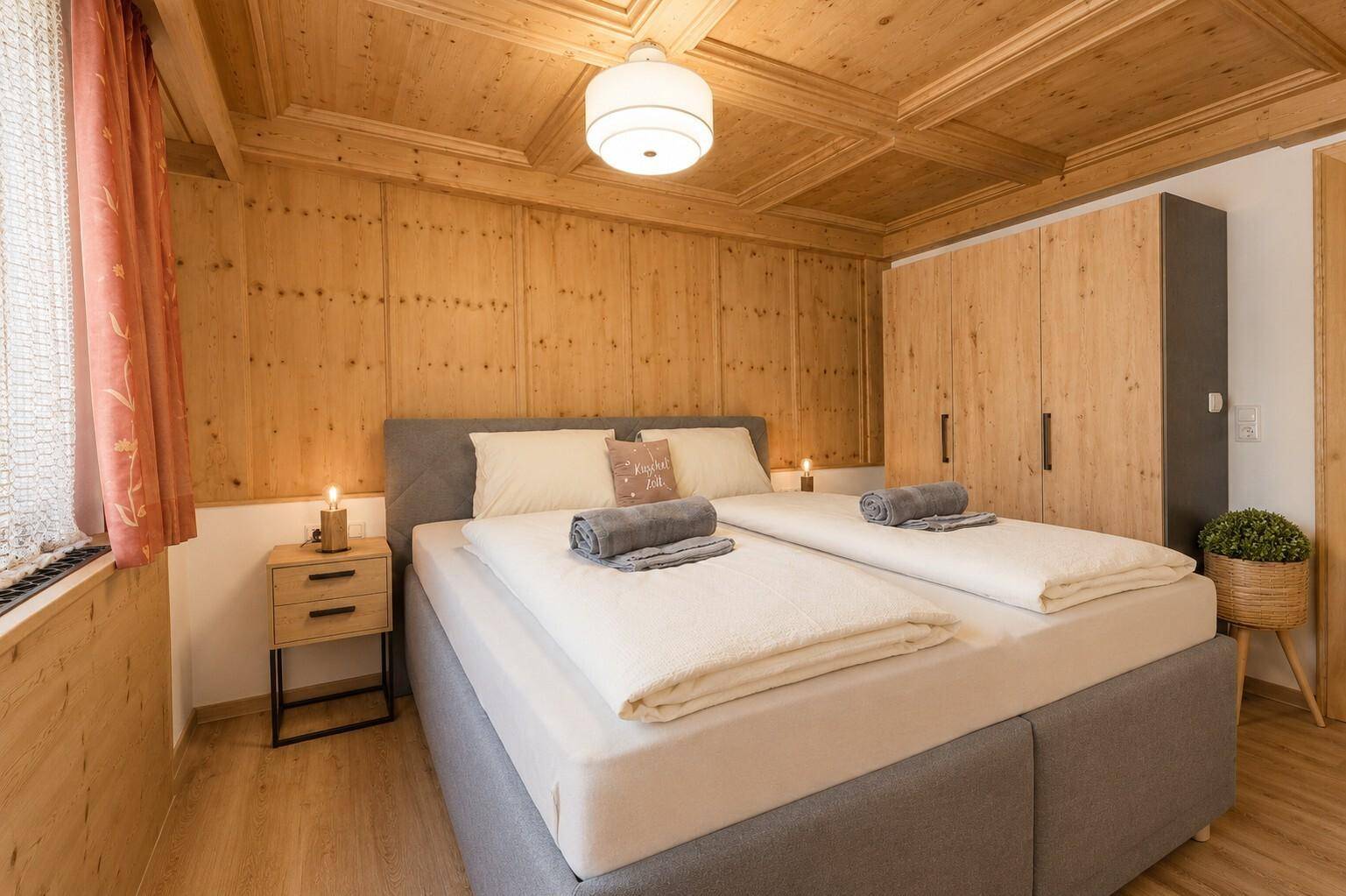 Schlafzimmer im alpinen Stil mit Holzwänden, Holzkassettendecke und Doppelbett.