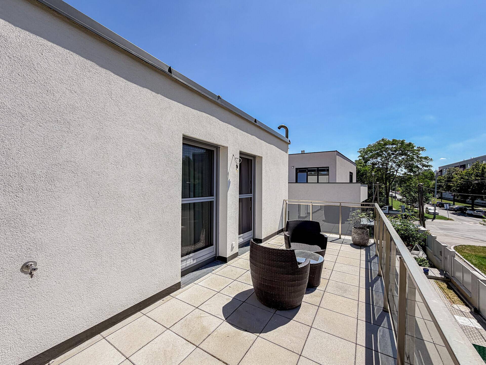 Großer Balkon mit Fliesenboden, Glasgeländer und Sitzgelegenheiten.