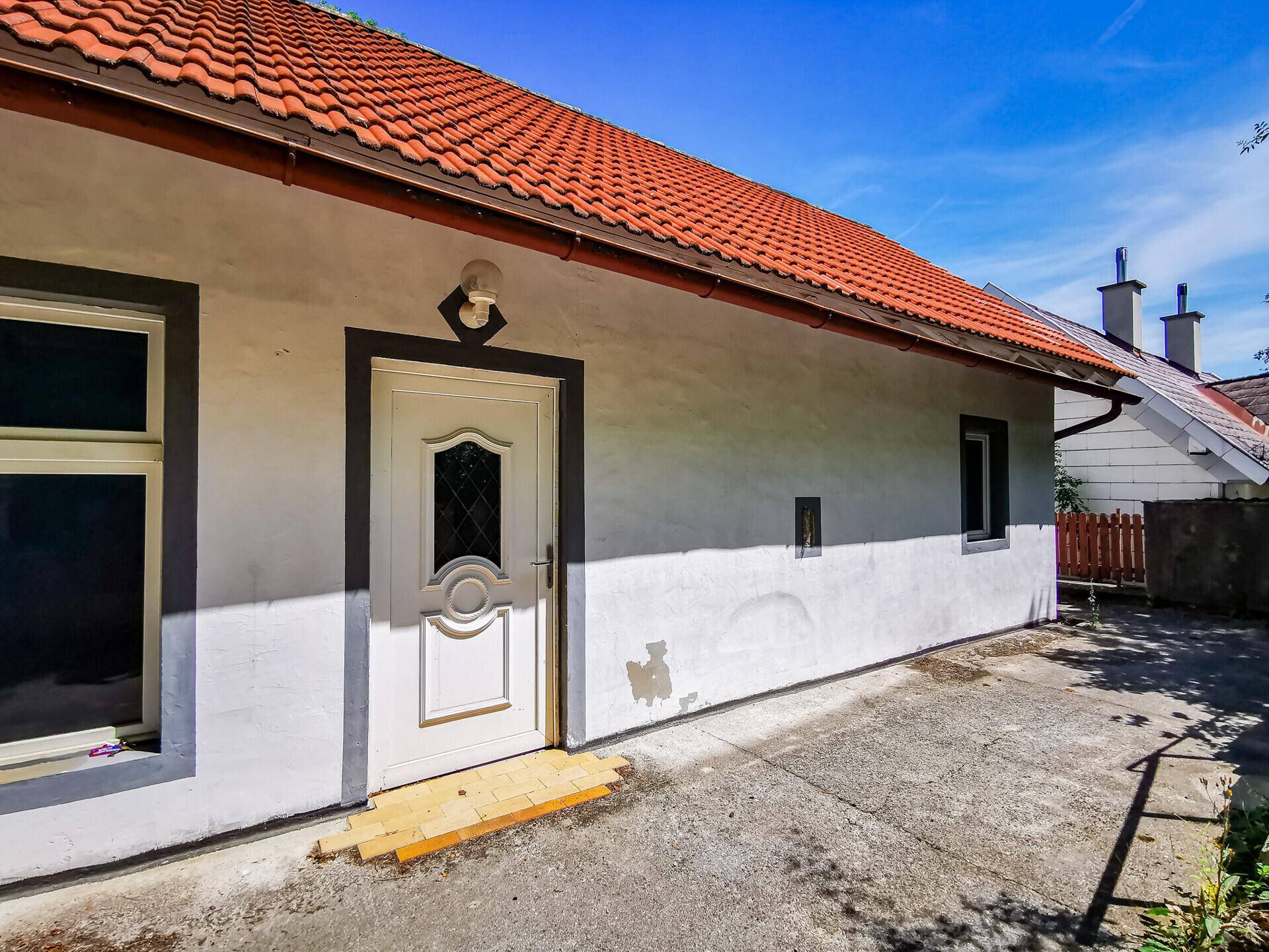 Weiße Hausfassade mit rotem Ziegeldach und einer weißen Eingangstür mit Glasausschnitt.