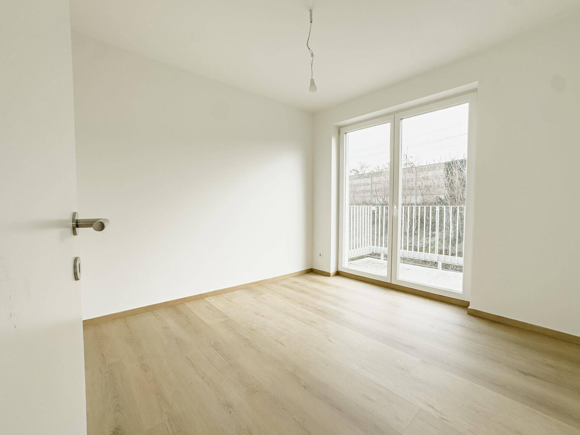 Helles Schlafzimmer mit Holzboden und großem Fenster, das einen französischen Balkon bietet.
