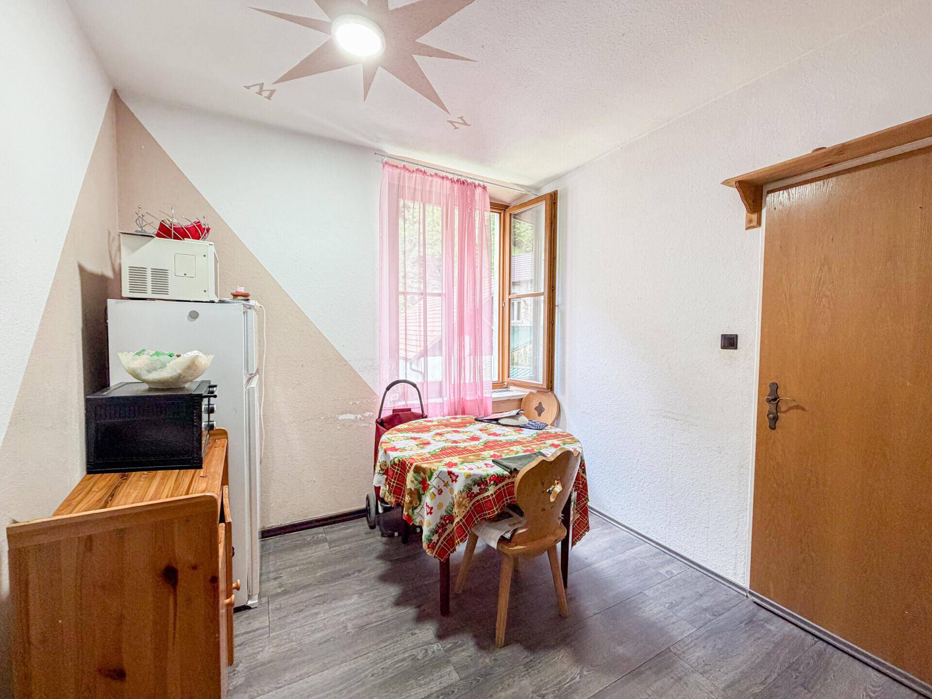 Kleine Küche mit Esstisch, Kühlschrank und farbiger Wandgestaltung.