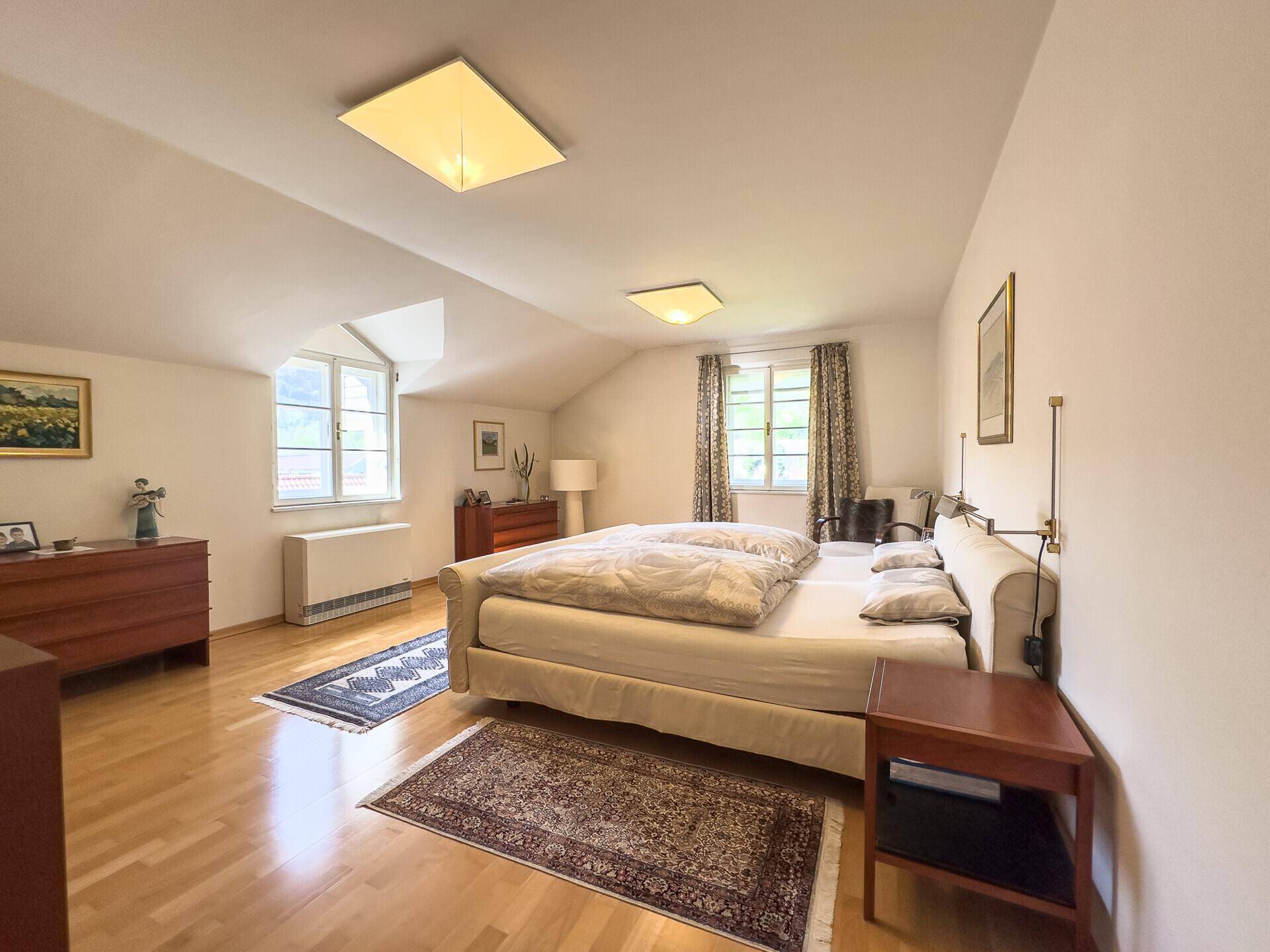 Helles Schlafzimmer mit Holzboden, Doppelbett und Fenstern mit Blick ins Grüne.