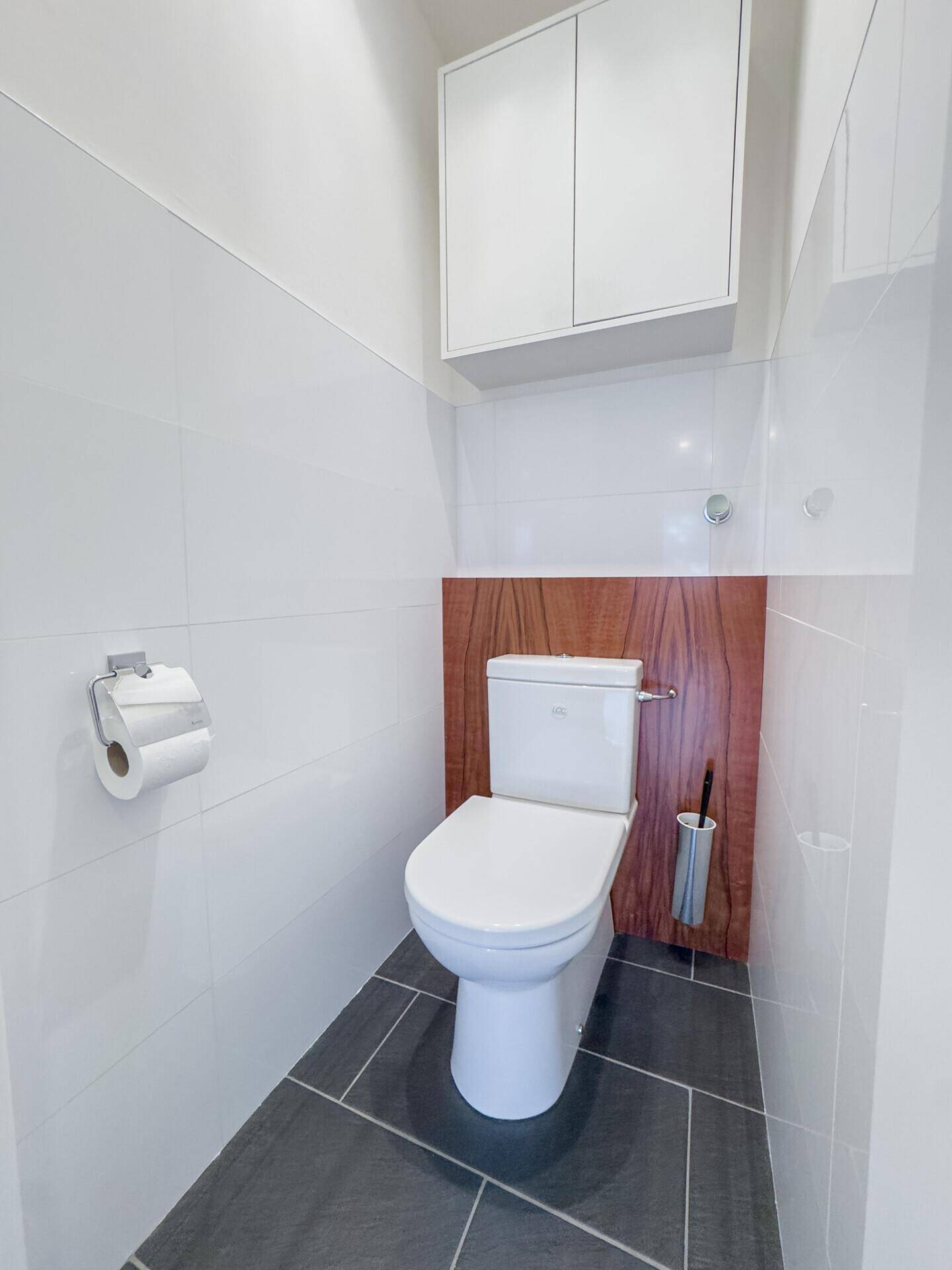 Separates Gäste-WC mit Wand-WC, weißen Fliesen und dunklem Fliesenboden.