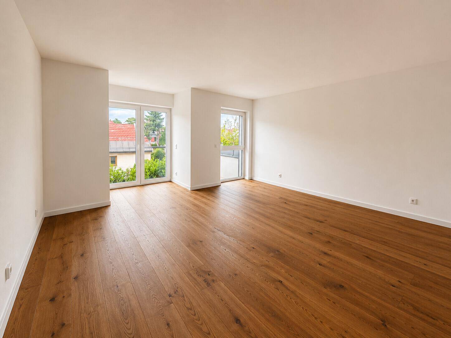 Heller Wohnbereich mit Holzboden und zwei großen Glastüren, die ins Freie führen.