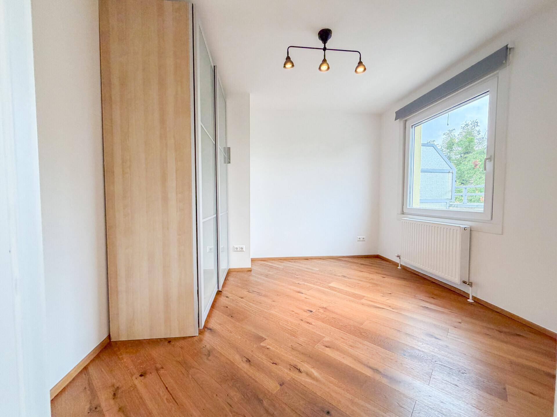 Schlafzimmer mit Holzboden, großem Kleiderschrank und Fenster für natürliches Licht.