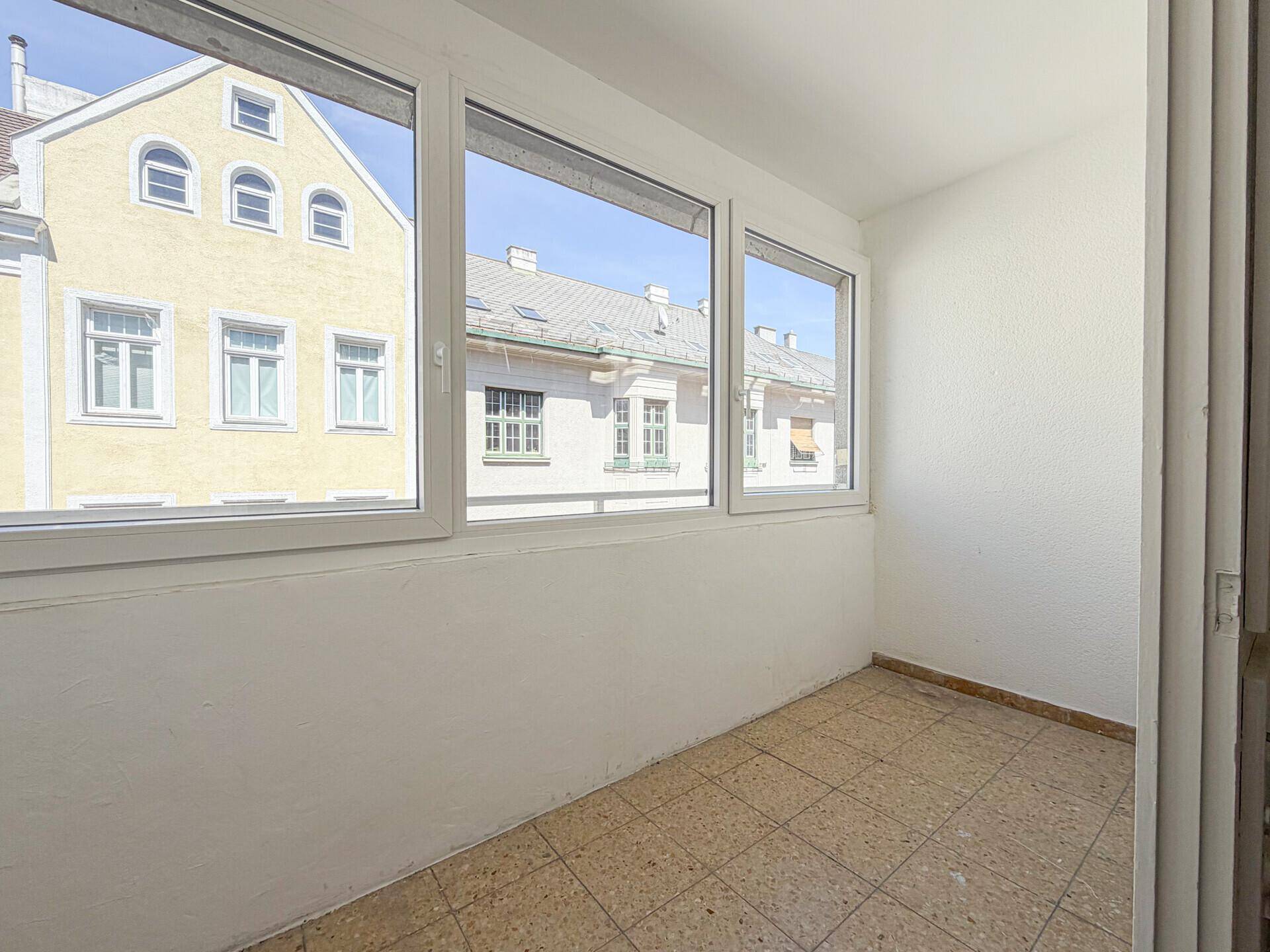 Geschlossene Loggia mit Fliesenboden und weitem Blick auf die umliegenden Gebäude.