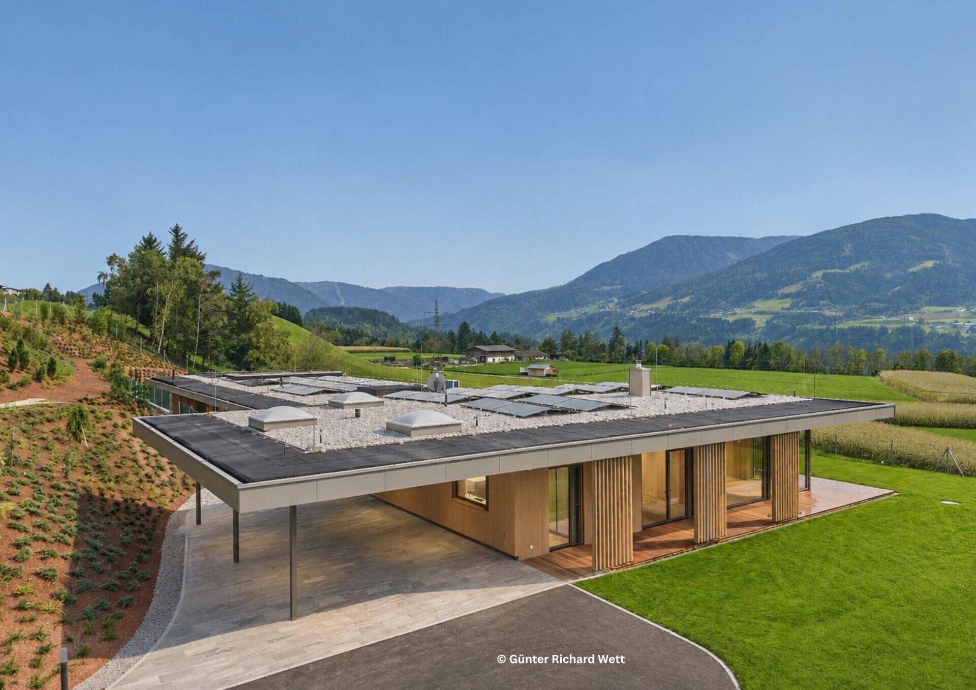 Elegantes Einfamilienhaus mit Flachdach, Carport und Solarpaneelen in ländlicher Umgebung.