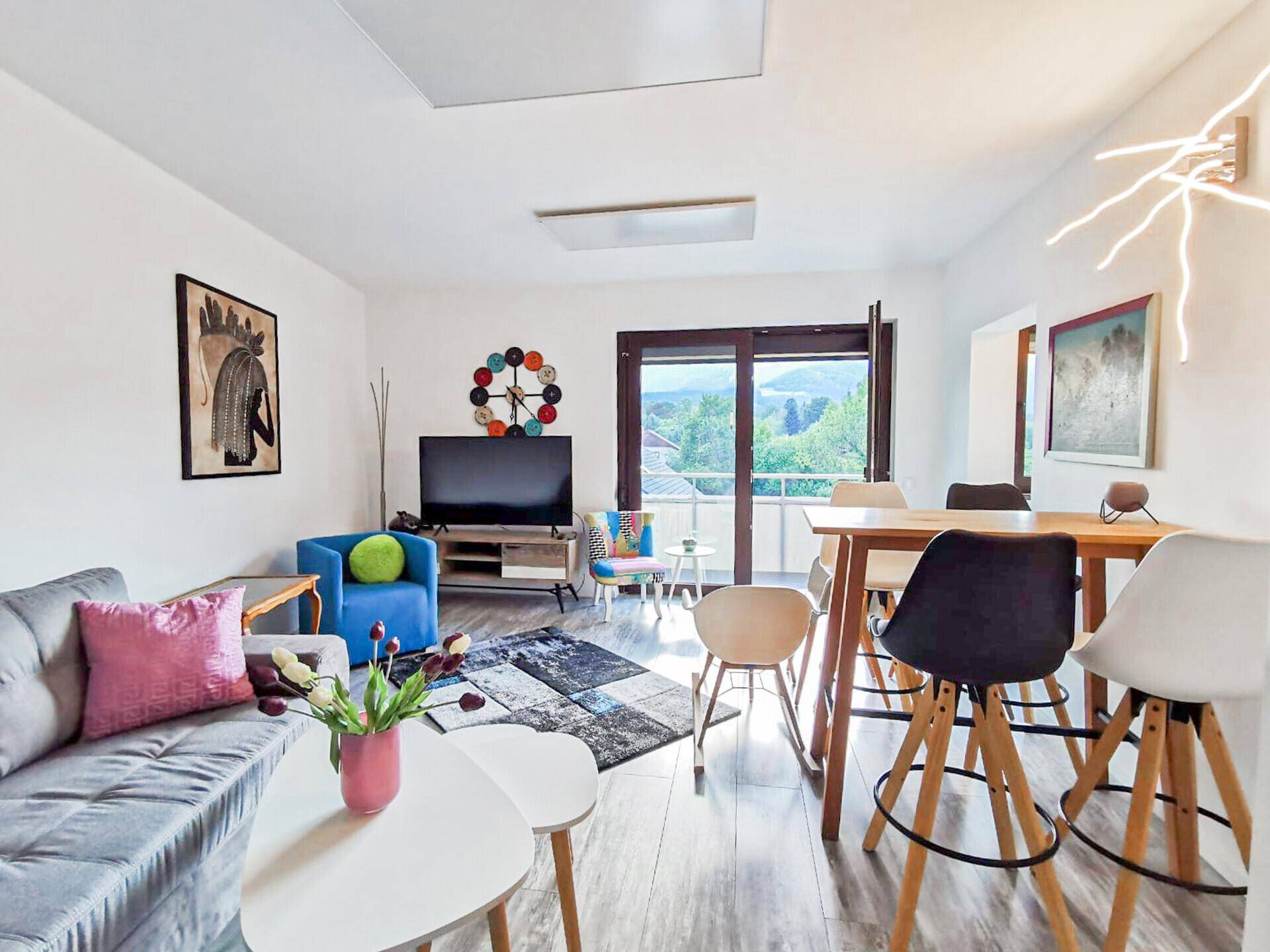 Gemütlicher Wohn- und Essbereich mit Sofa, Fernseher und Balkonzugang.