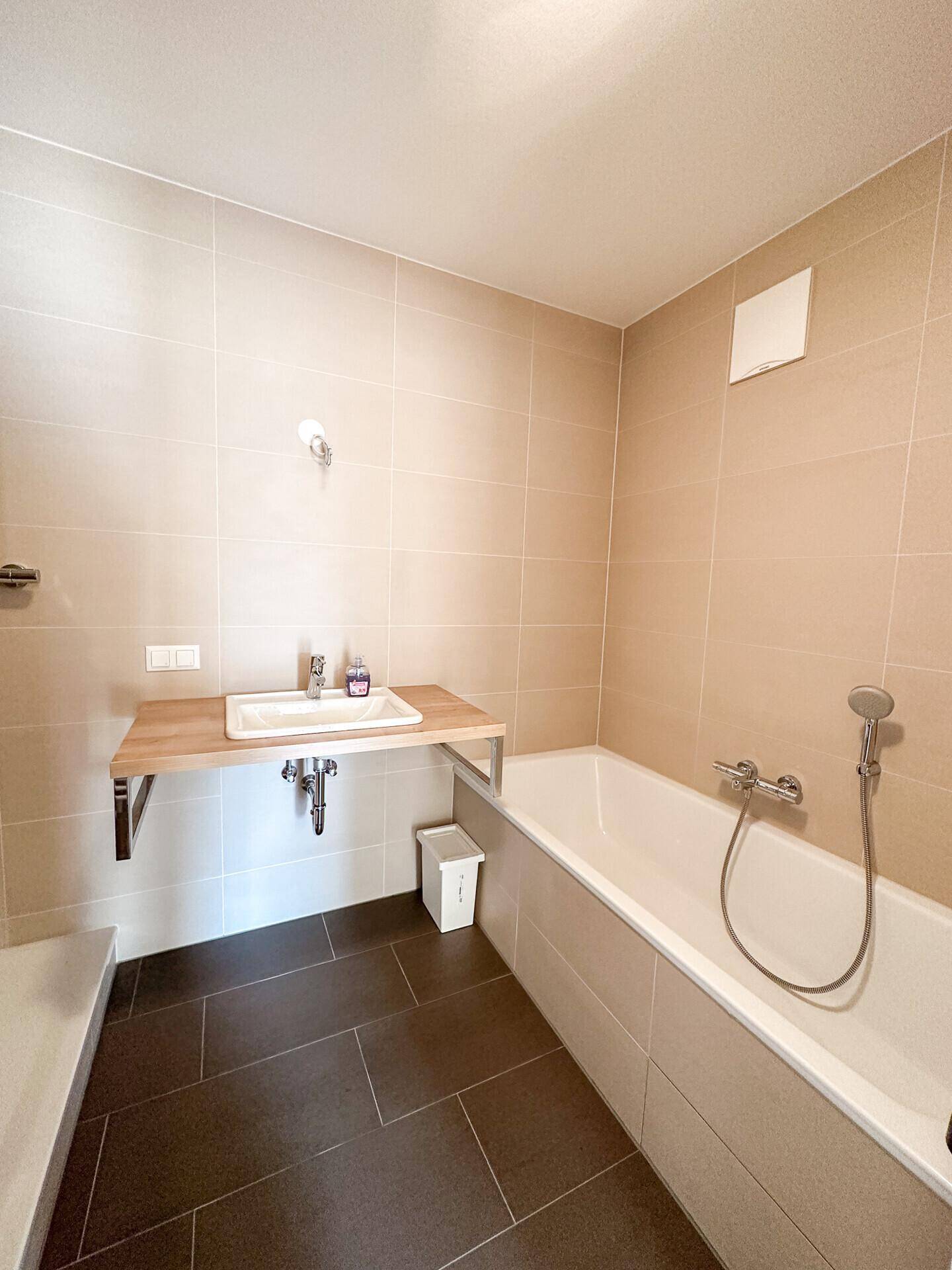 Helles Badezimmer mit Badewanne, Einzelwaschbecken und beigefarbenen Fliesen.