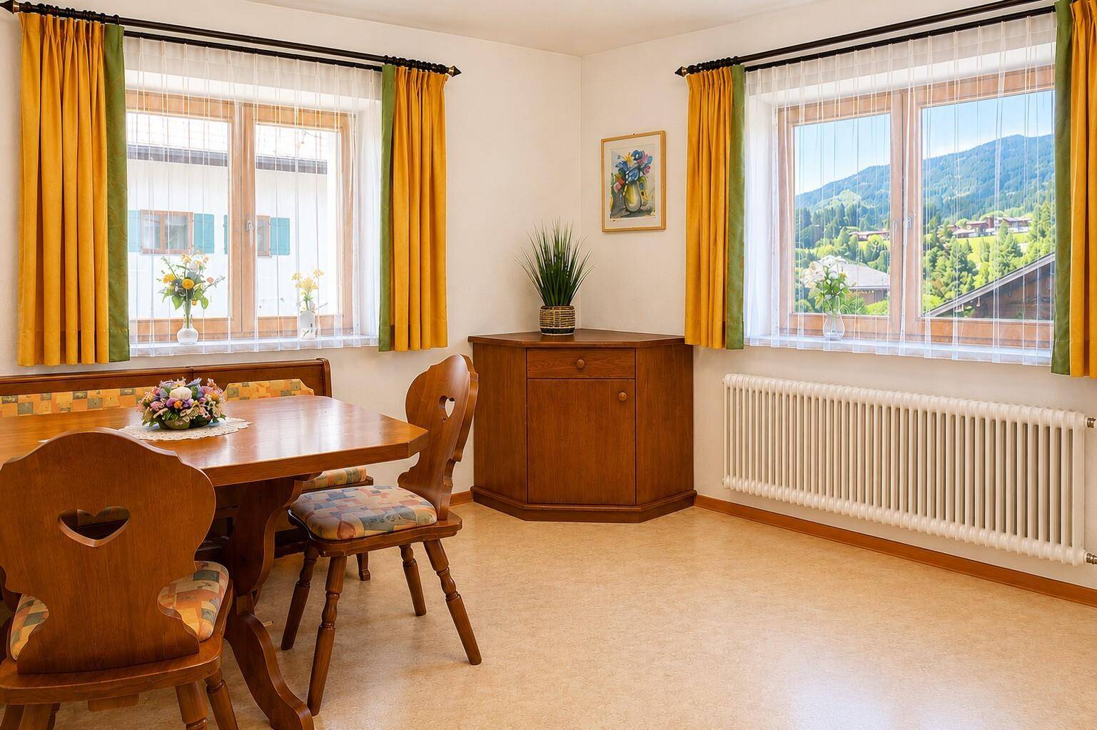 Heller Essbereich mit traditionellen Holzmöbeln, Eckbank und Fenstern mit Bergblick.