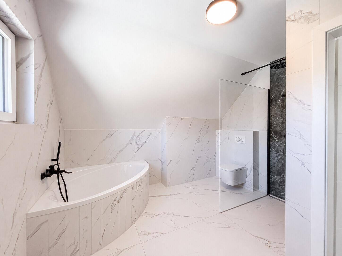 Elegantes Badezimmer im Dachgeschoss mit Badewanne, begehbarer Dusche und Marmorfliesen.