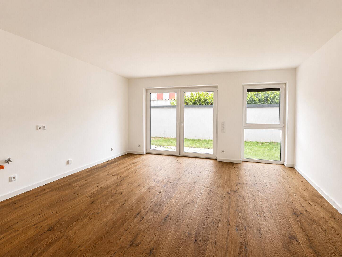 Lichtdurchfluteter Raum mit Holzboden und großen Fenstern, die den Blick ins Grüne freigeben.
