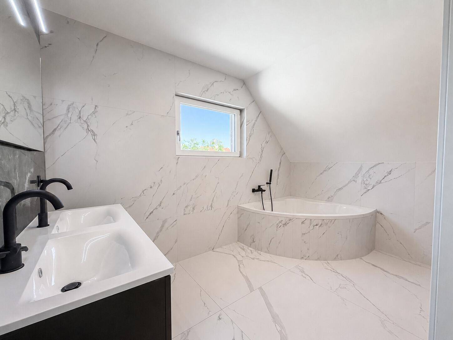 Modernes Badezimmer im Dachgeschoss mit Marmorfliesen, Badewanne und Dachfenster.