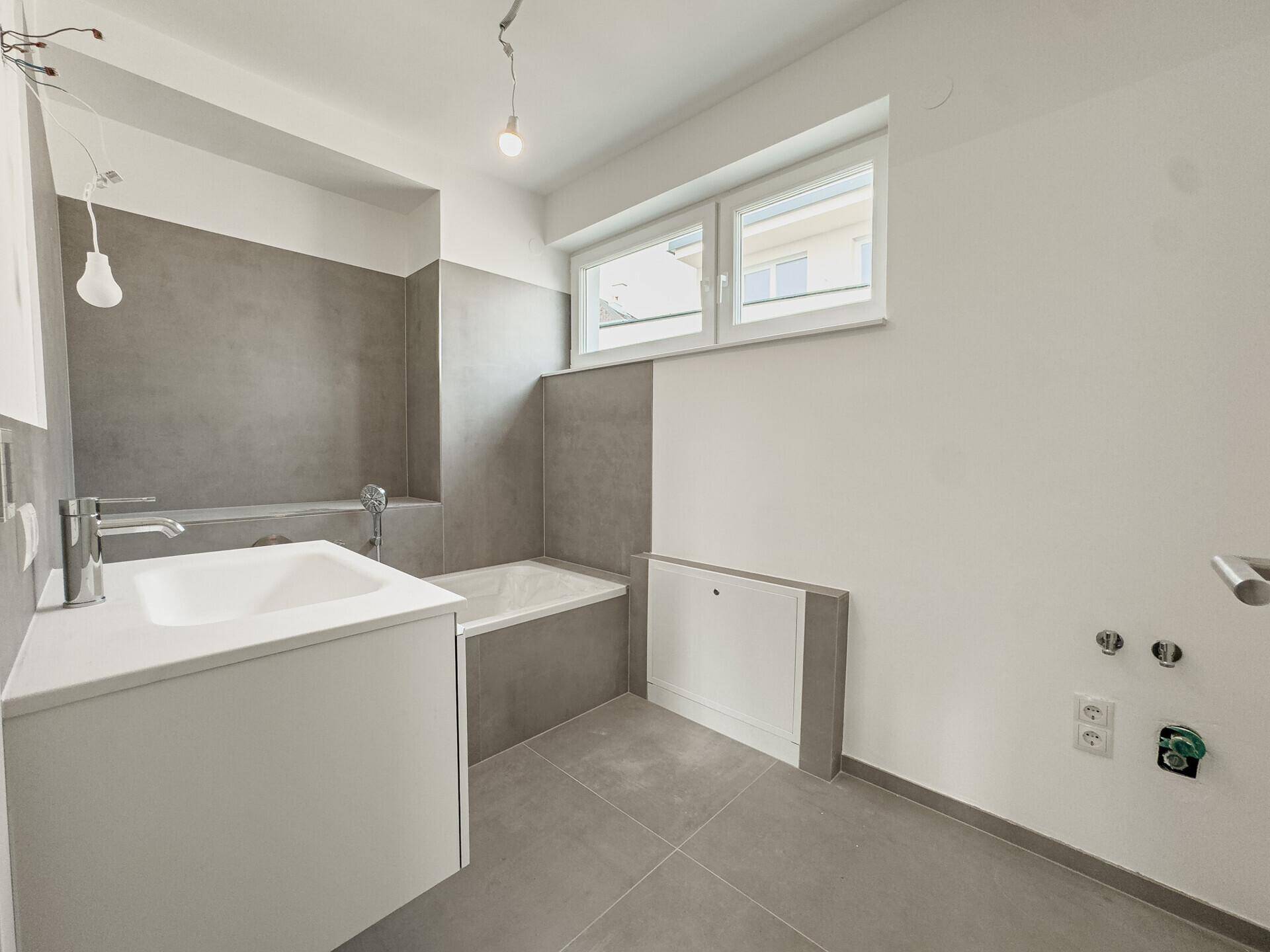 Modernes Badezimmer mit Badewanne, Waschbecken und grauen Fliesen, bereit für die Einrichtung.