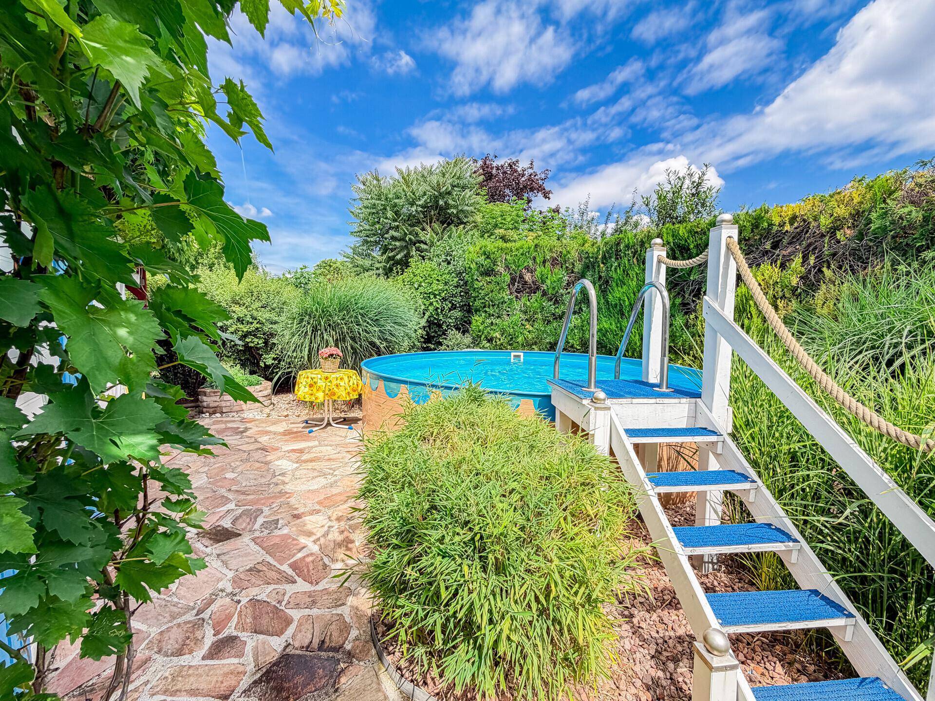 Detailansicht des Aufstellpools mit Holzverkleidung und angrenzendem Steinplattenweg.