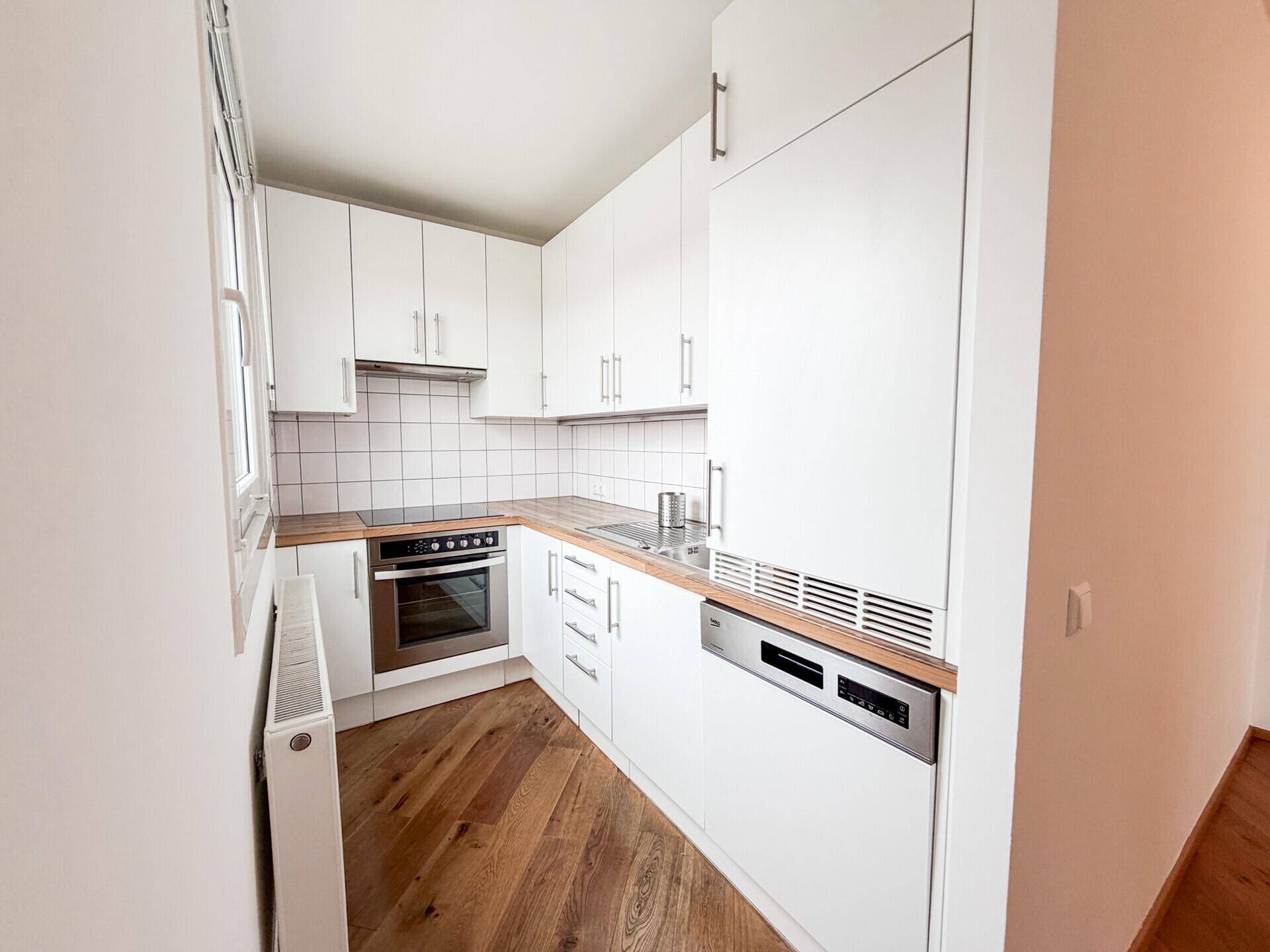 Moderne Einbauküche mit weißen Schränken, Holztheke und integrierten Geräten.
