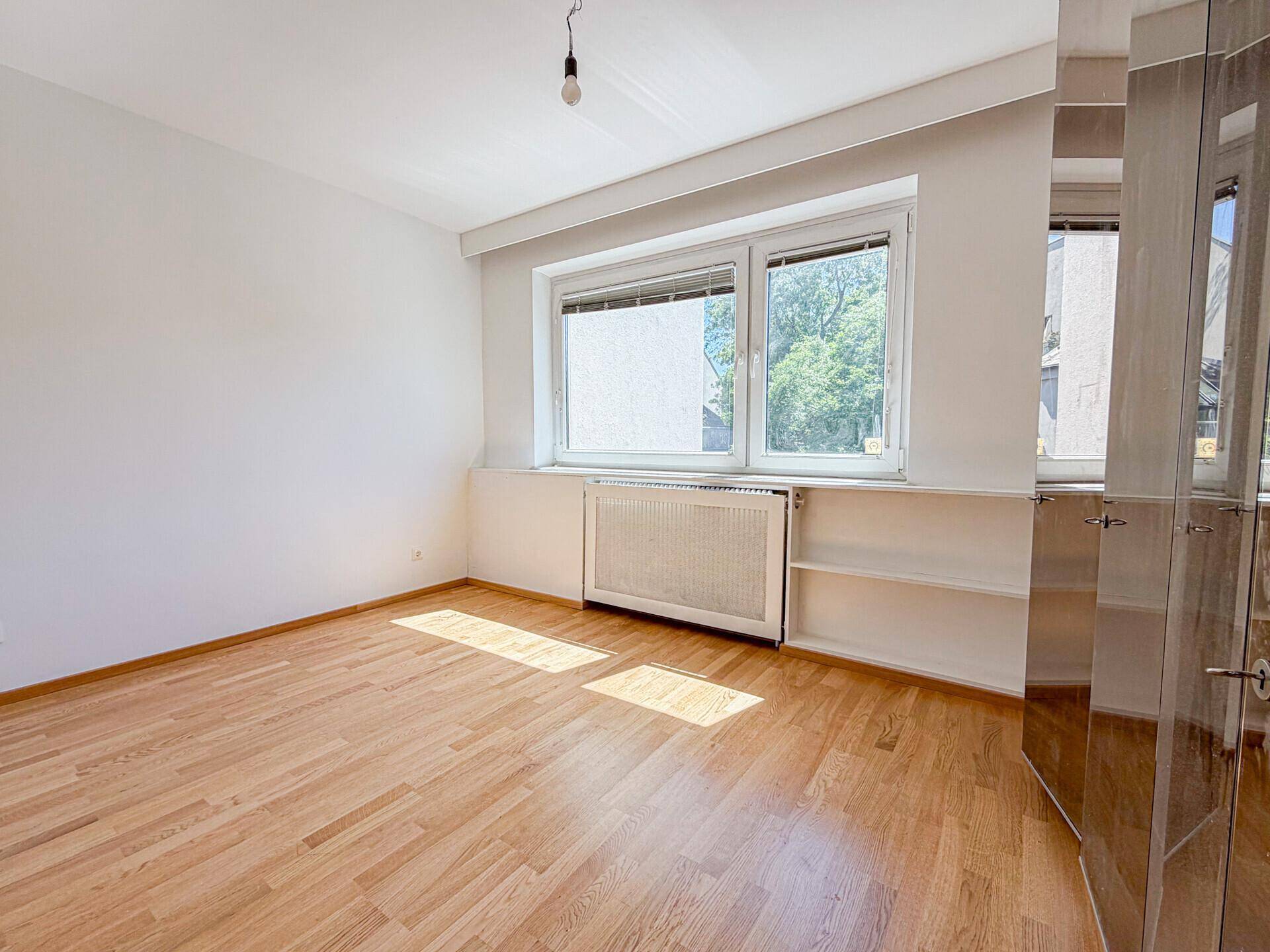 Schlafzimmer mit Parkettboden, großen Fenstern und einem integrierten Spiegelschrank.