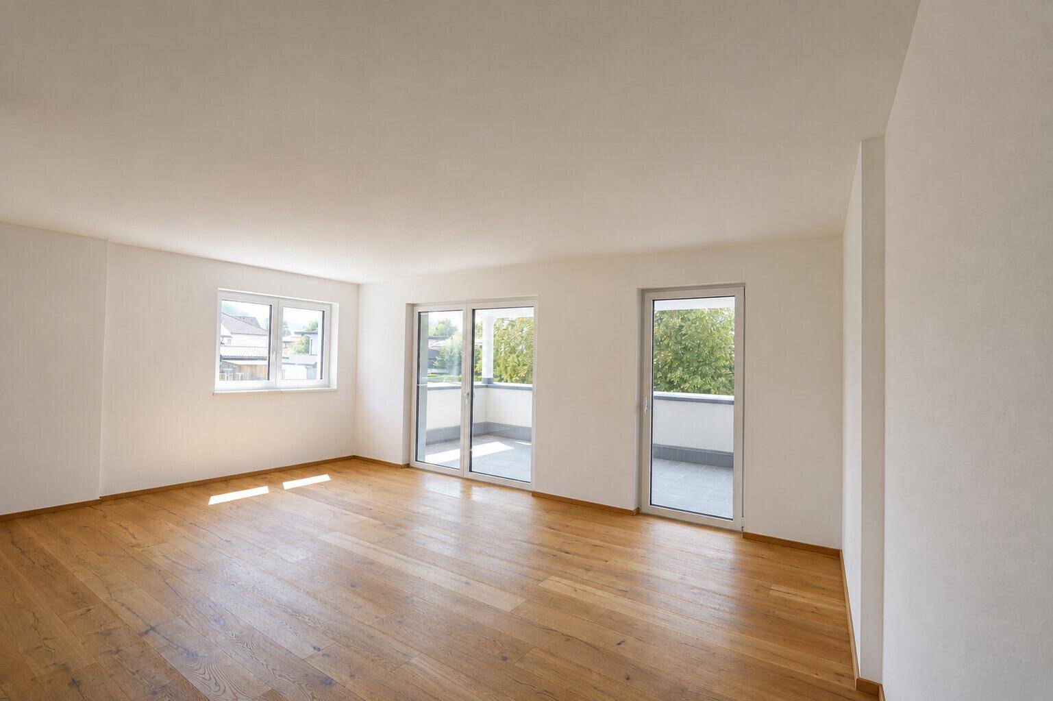 Heller, leerer Raum mit Holzboden, großen Fenstern und Zugang zu einem Balkon.