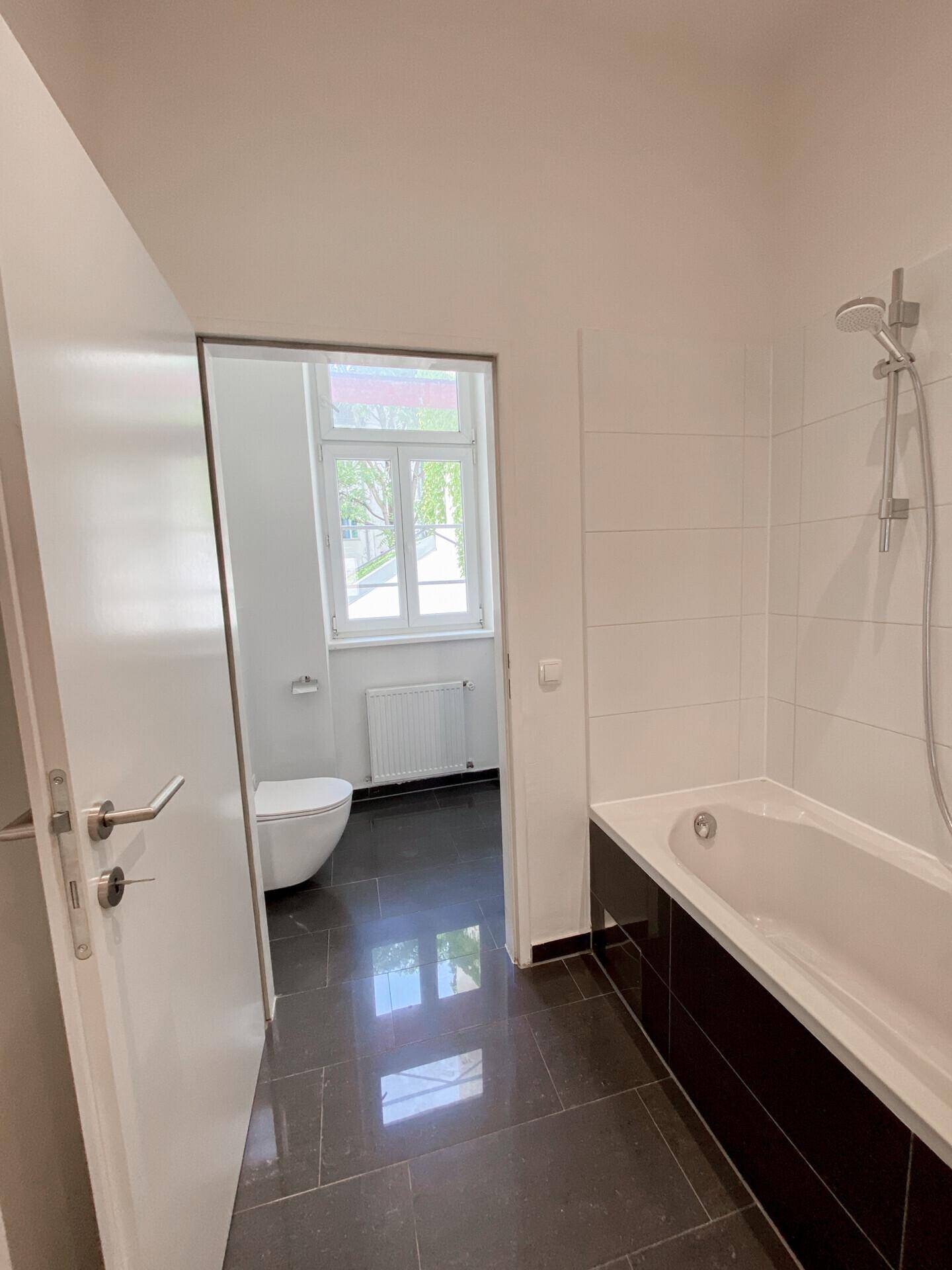 Helles Badezimmer mit Badewanne und Blick in den separaten WC-Bereich.