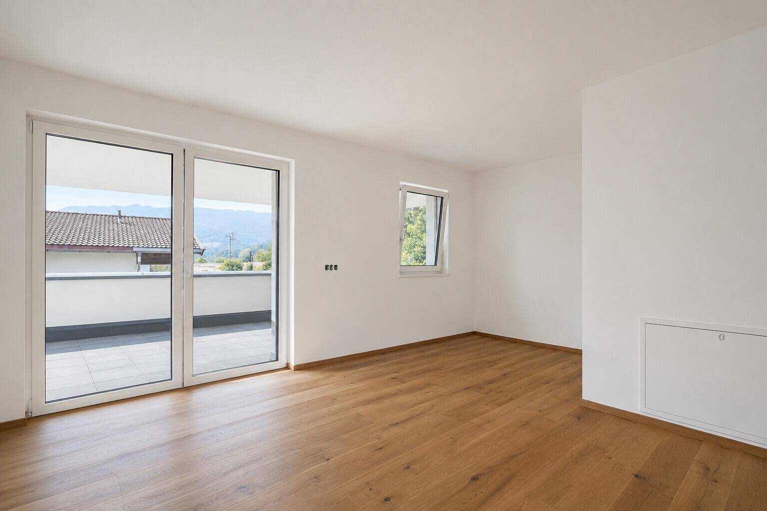 Heller Raum mit Holzboden und Zugang zu einer Terrasse mit Bergblick.