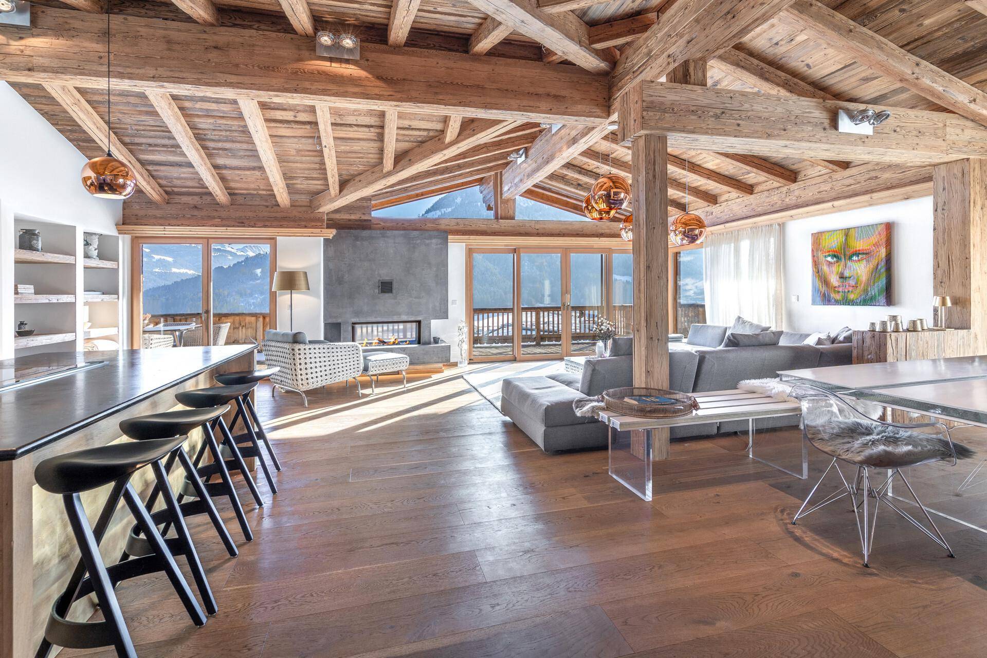 Heller Wohnbereich mit modernem Kamin, Holzboden und beeindruckendem Bergblick durch große Fenster.