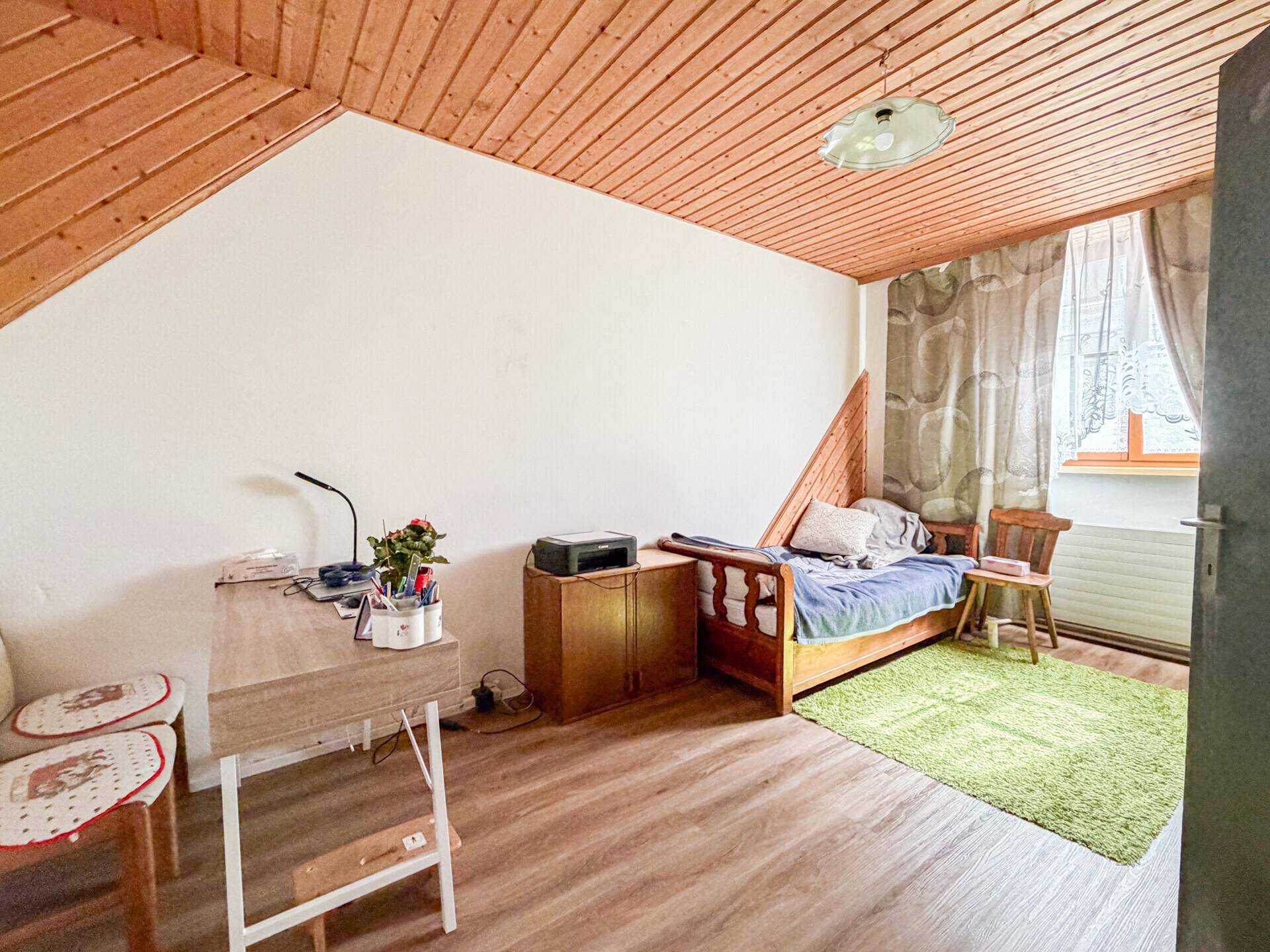 Gemütliches Schlafzimmer mit Holzdachschrägen, Laminatboden und einem Einzelbett.