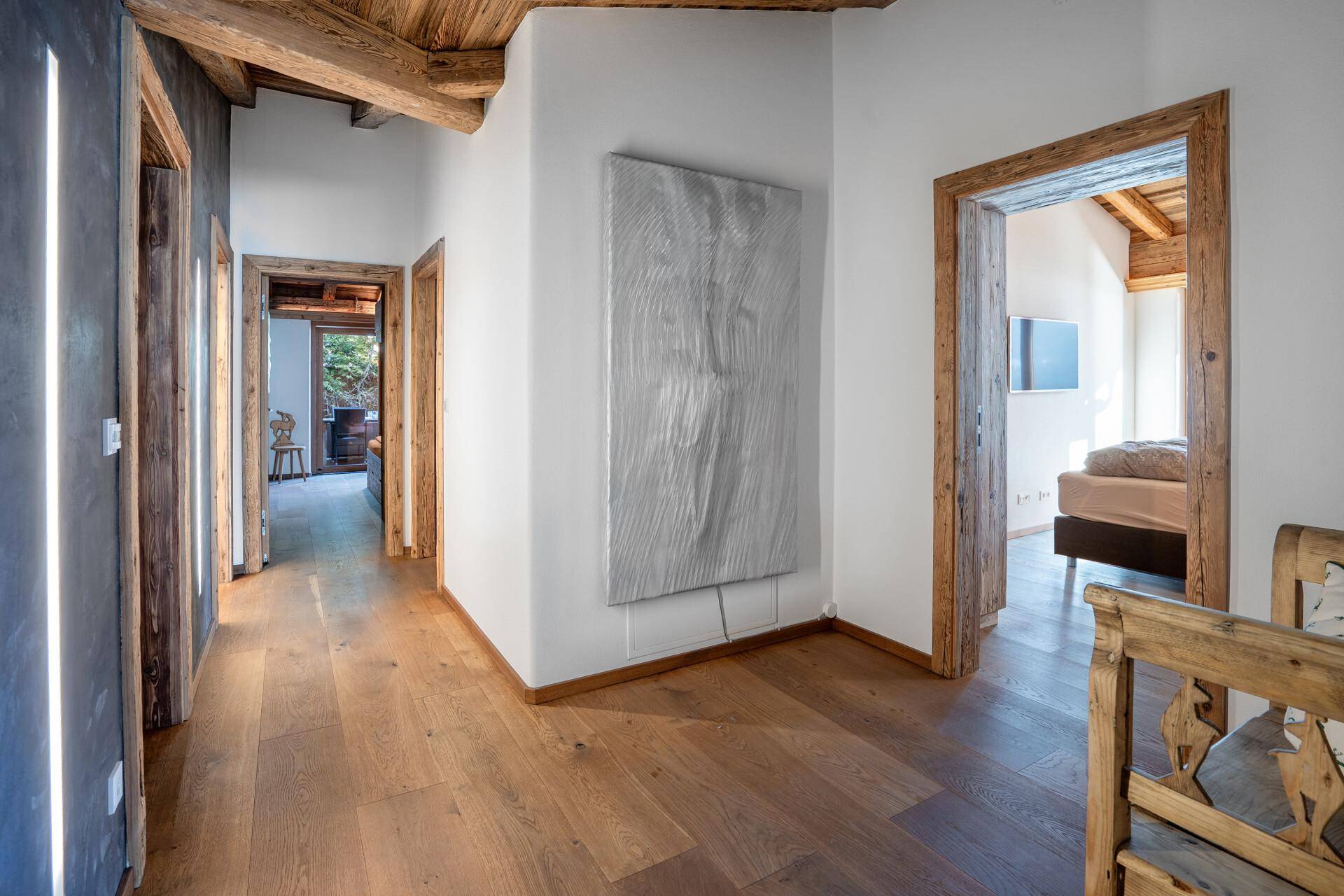 Heller Flur mit Holzboden, weißen Wänden und modernem Kunstwerk, der zu weiteren Räumen führt.