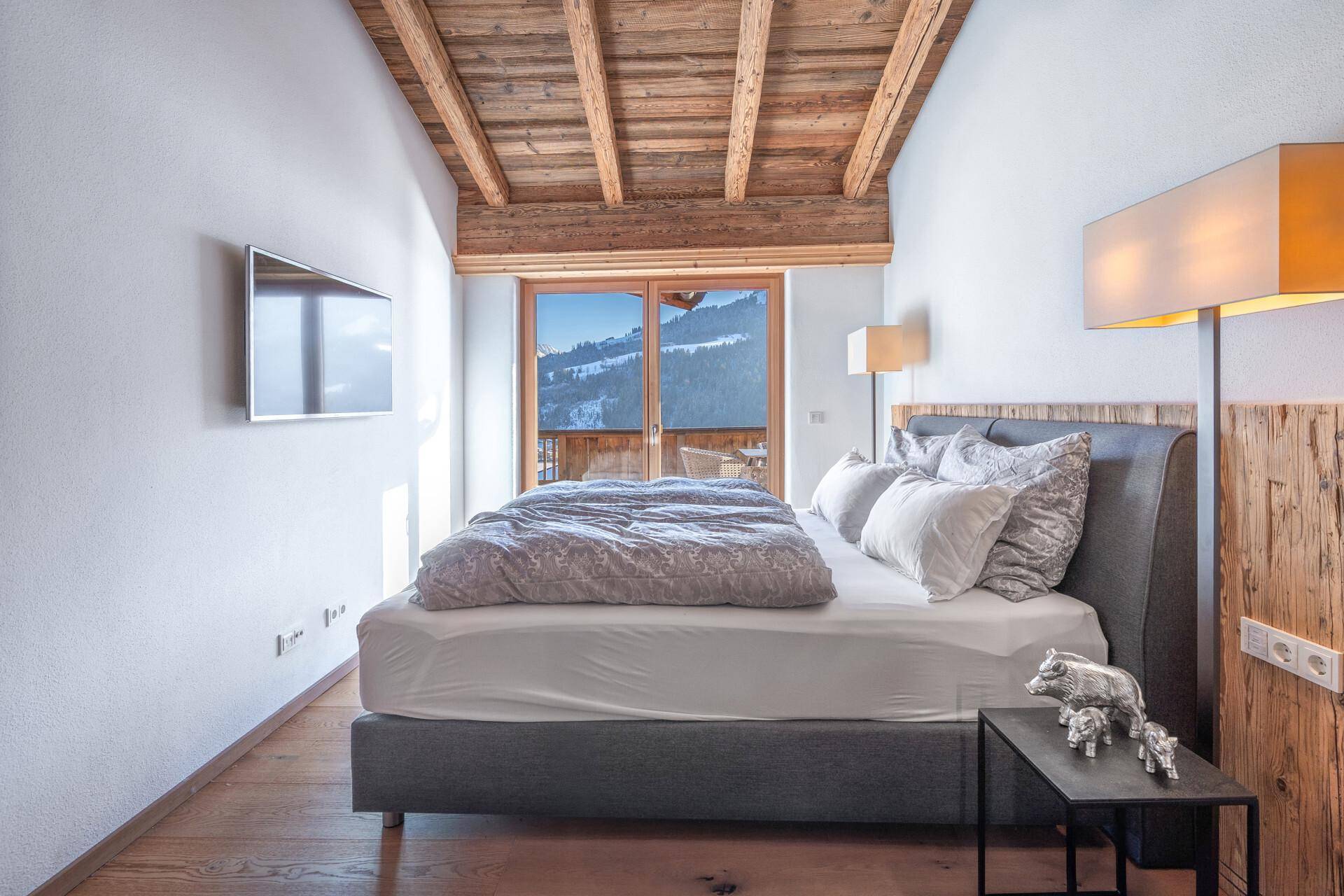 Helles Schlafzimmer mit Holzbalken, modernem Bett und malerischem Blick auf die verschneite Landschaft.