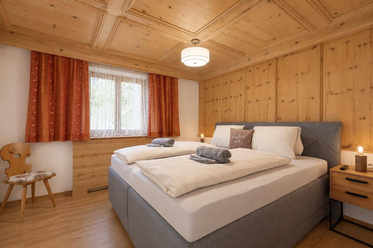 Helles Schlafzimmer mit Holzwänden, Holzkassettendecke und traditionellen alpinen Elementen.