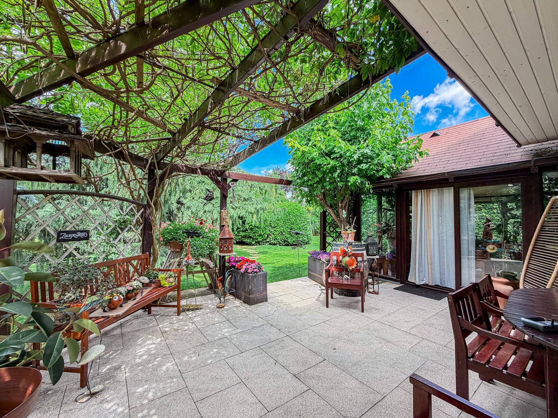 Überdachte Terrasse mit Holzbänken und Blick auf den grünen Gartenbereich.
