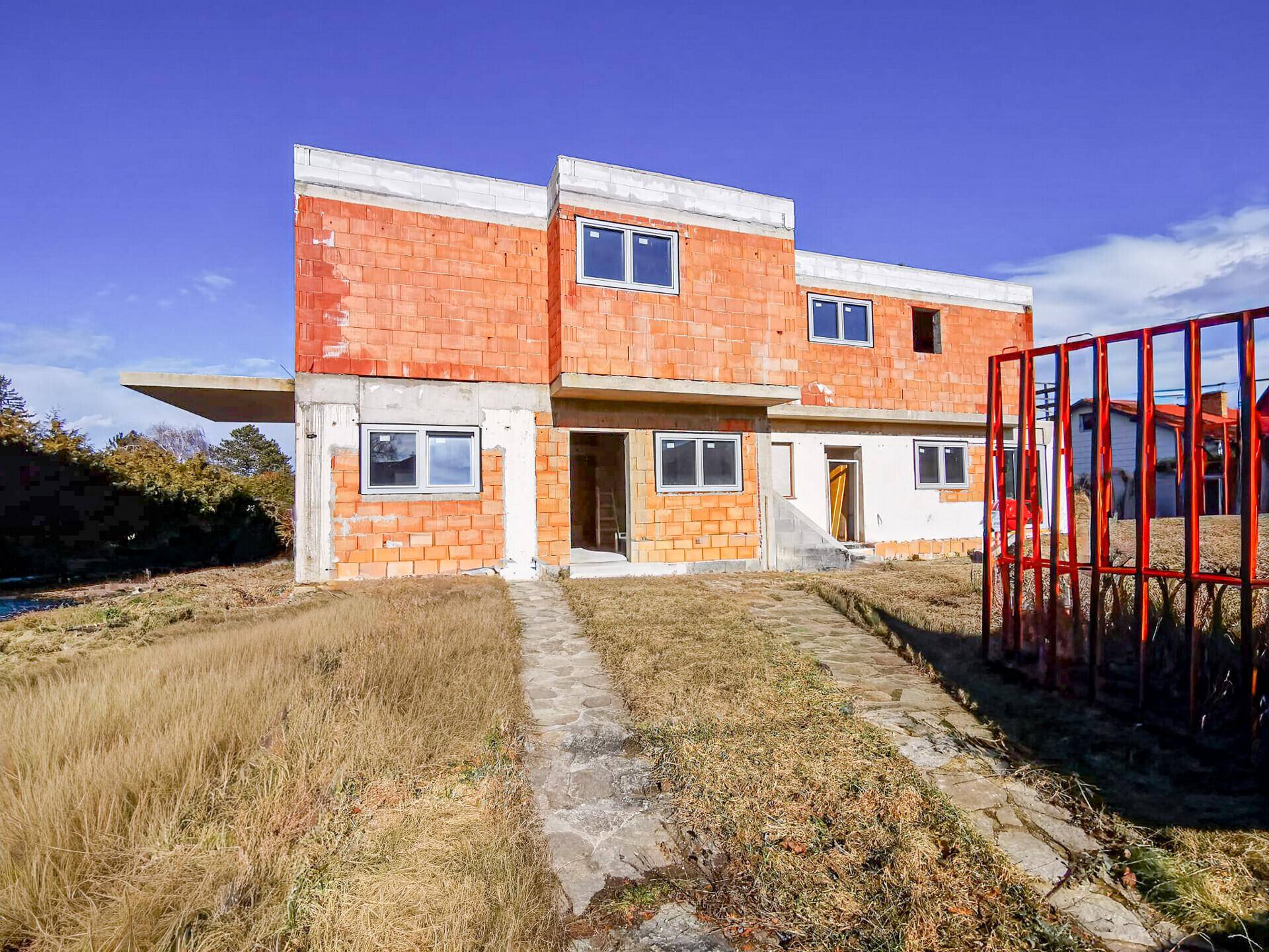Frontansicht des Rohbaus eines modernen Hauses mit neuen Fenstern und unverputzten Ziegelwänden.
